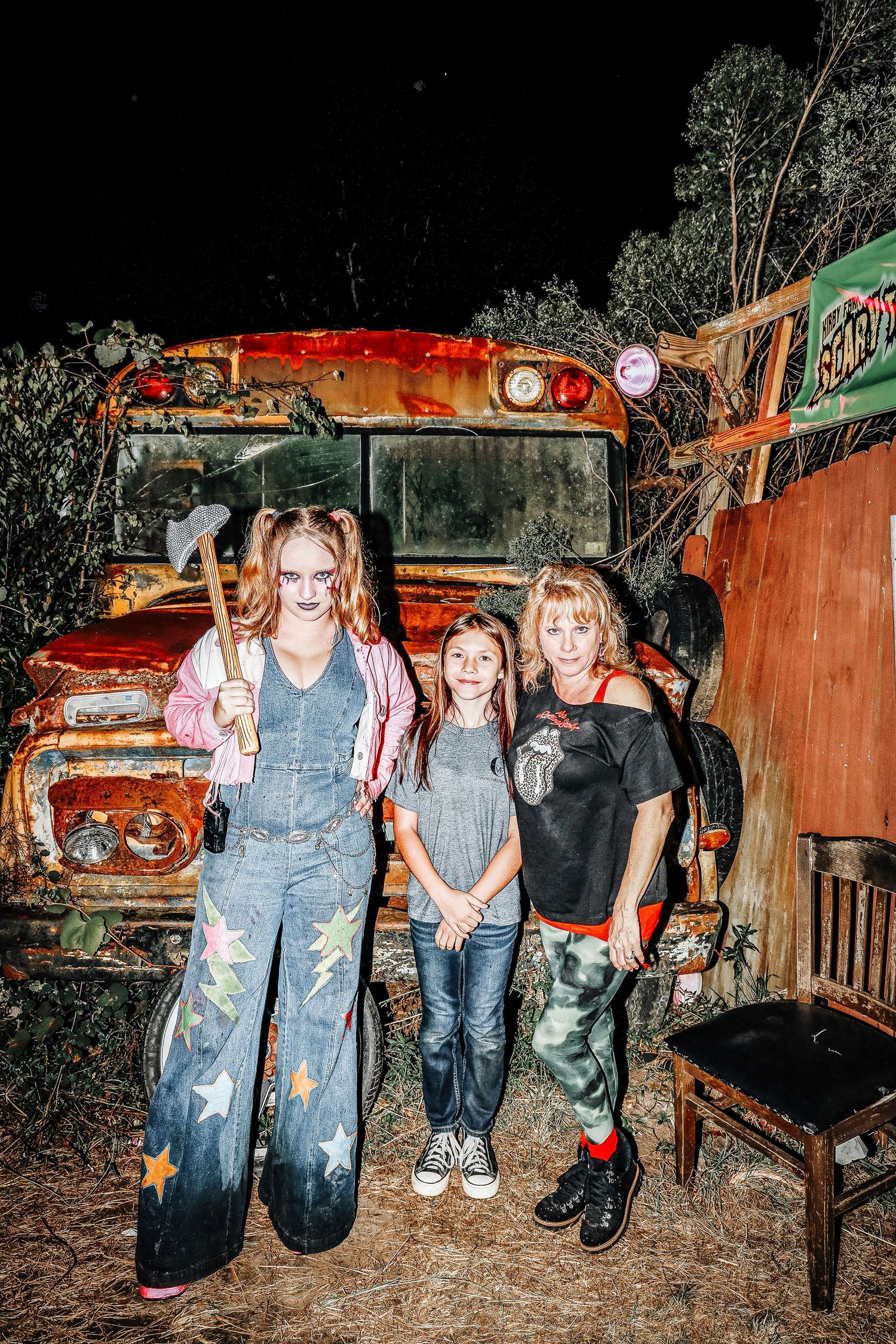 A group poses together in front of rustic orange vehicles at night wearing casual denim and dark clothing.