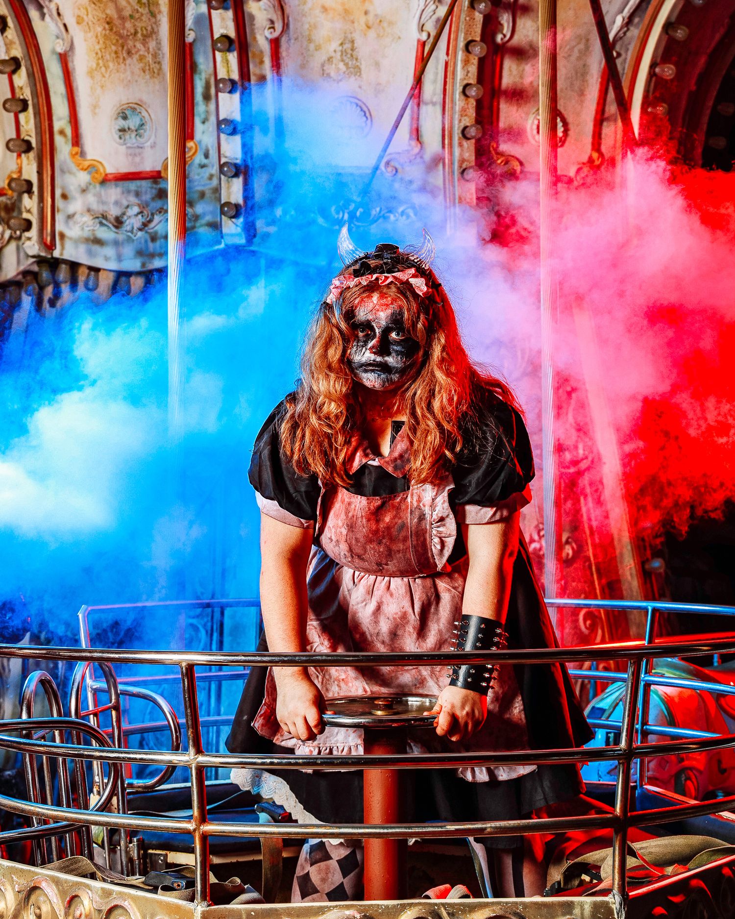 A person in a Halloween costume sits at a table surrounded by dramatic red and blue smoke effects.