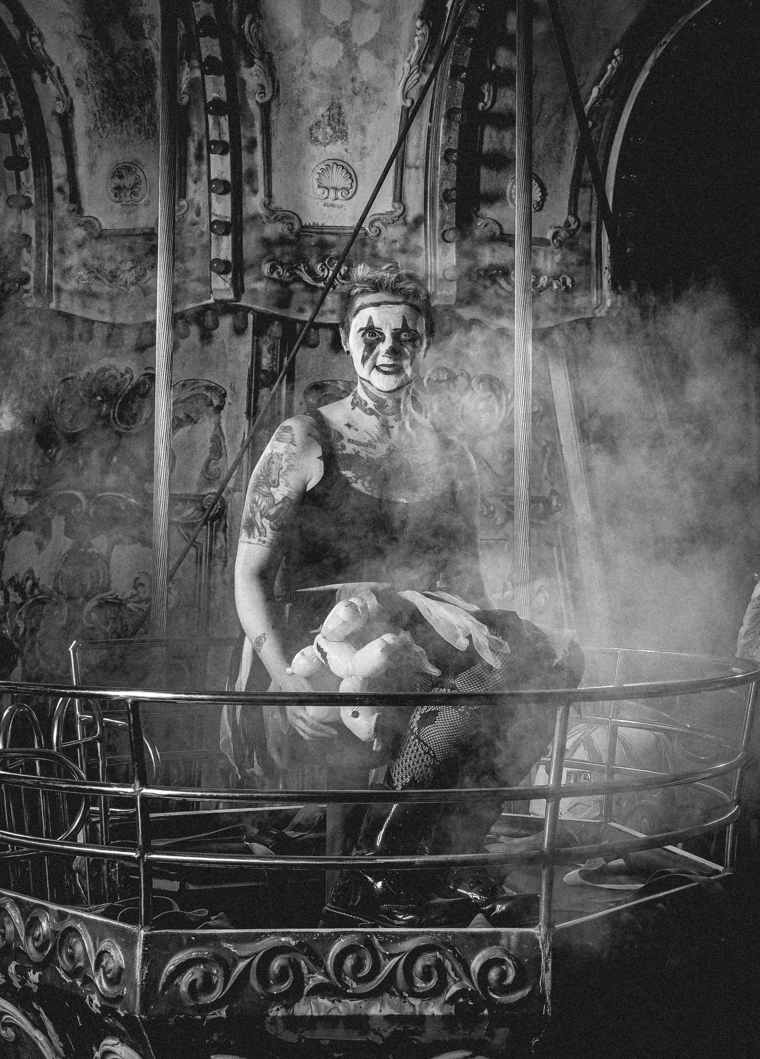 A creepy clown figure emerges from atmospheric fog in a vintage black and white carnival ride setting.