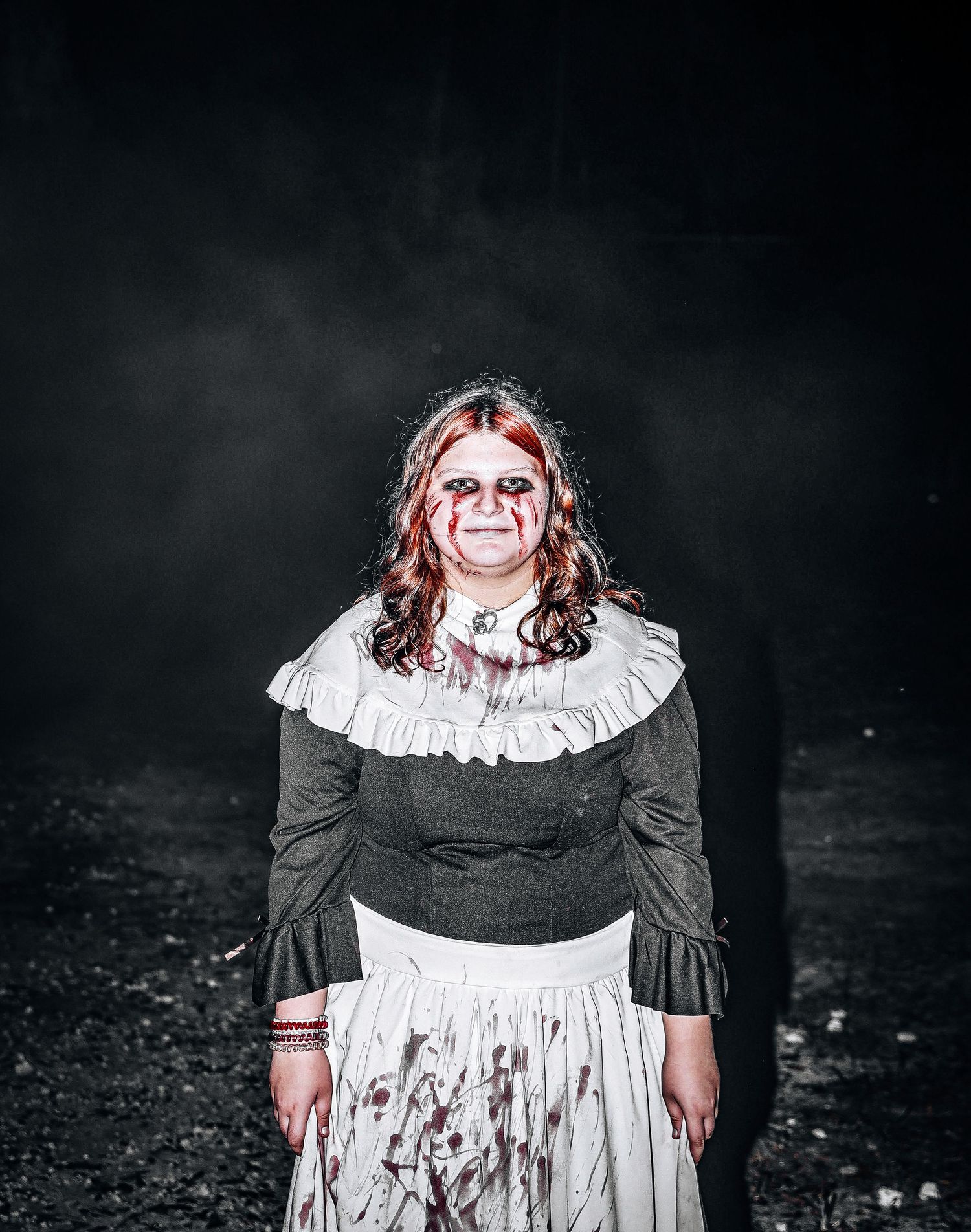 A haunting figure in Victorian-style dress and white ruffled collar stands against a dark background in a horror scene.