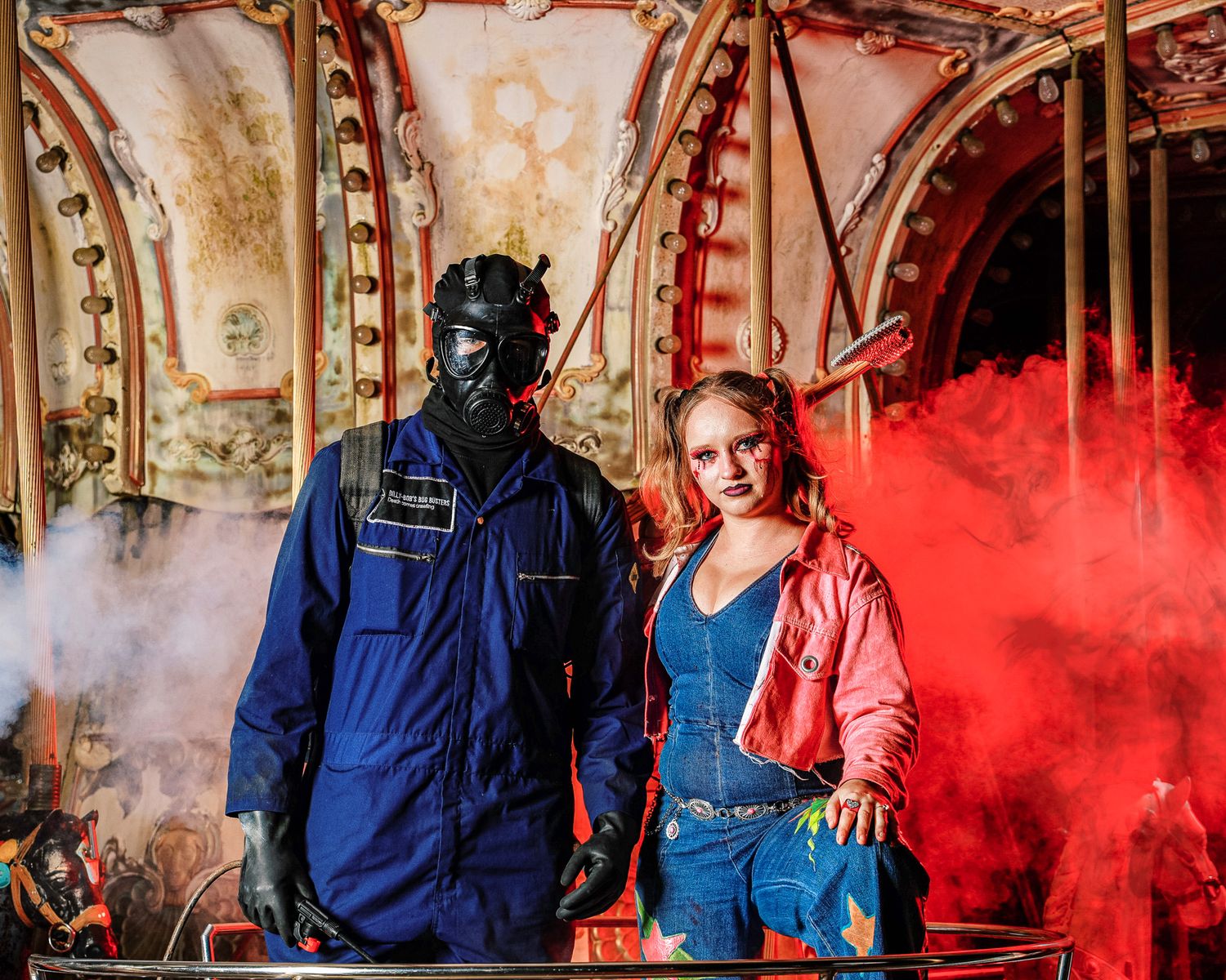 A dramatic carnival scene with colored smoke and two people in costume posing against vintage carousel details.
