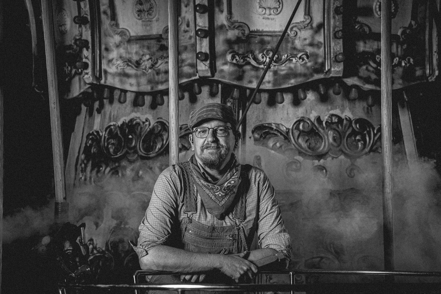 Black and white portrait of a person wearing a bandana and cap sitting at a counter with decorative background.