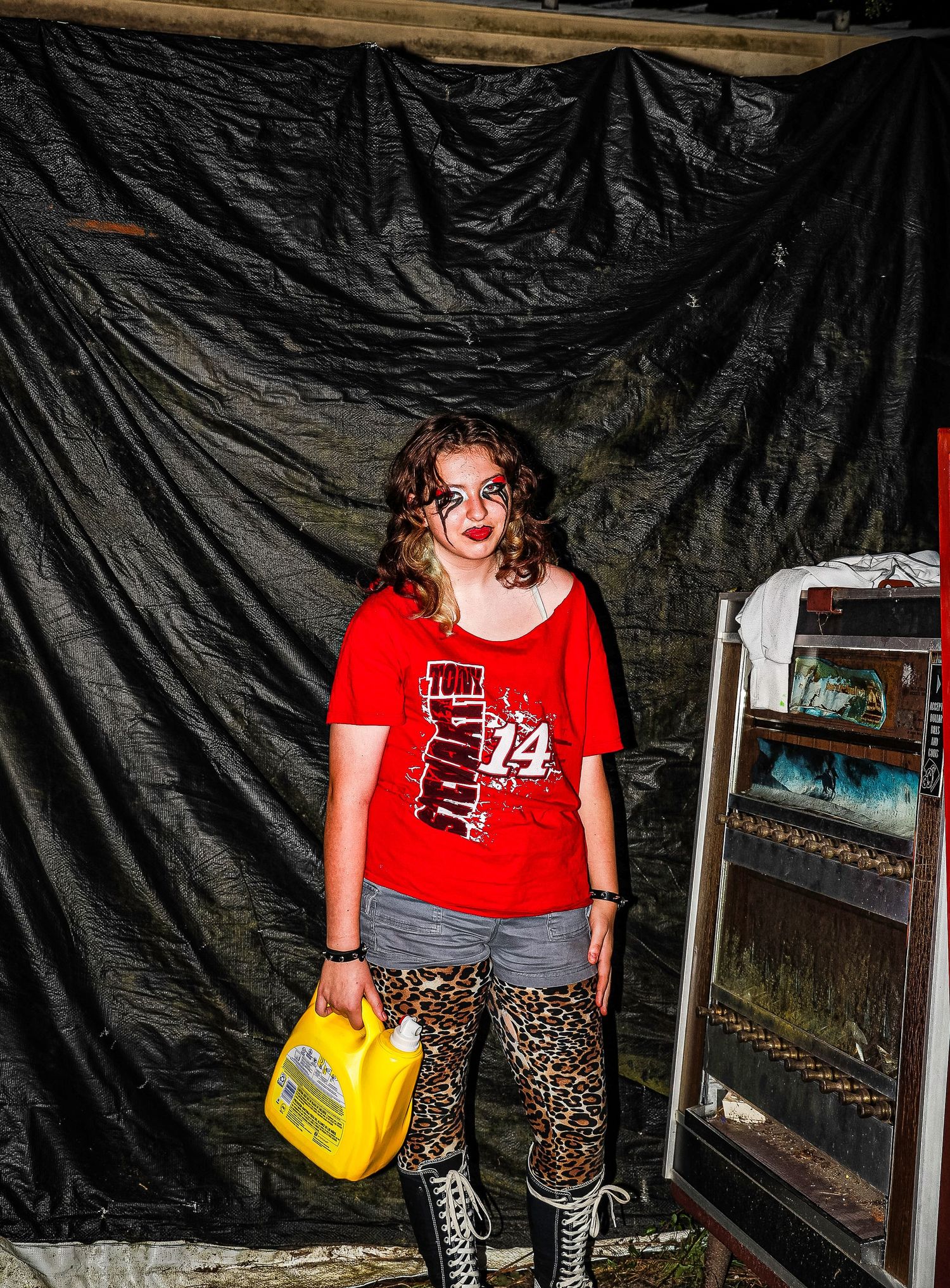 Person in red t-shirt and leopard print pants poses against black backdrop with yellow handbag and zebra print boots.