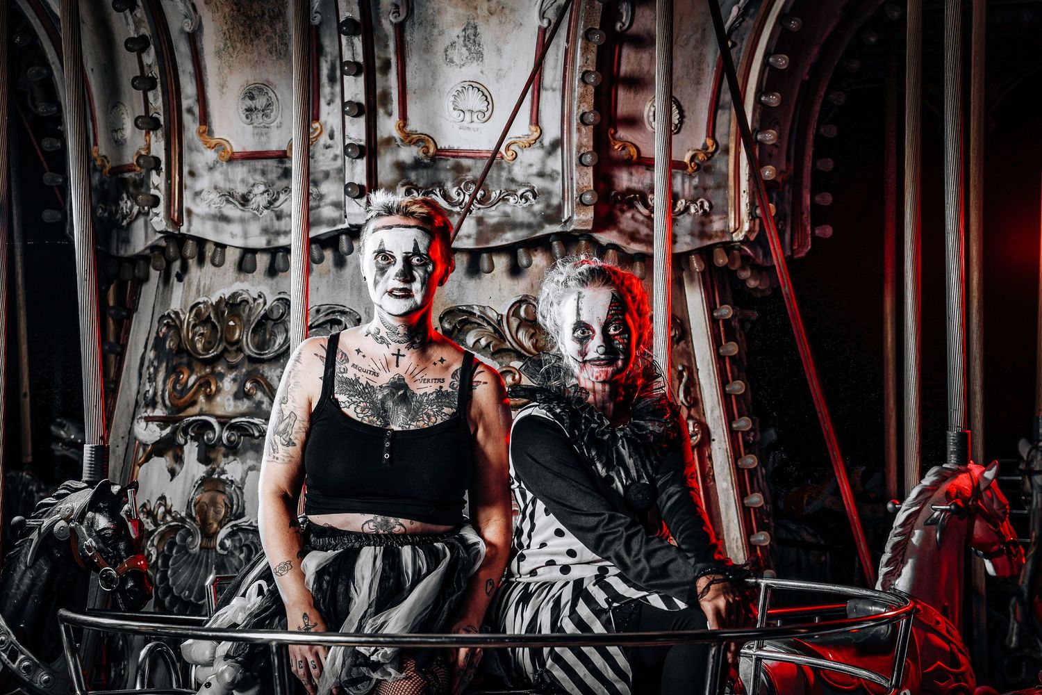 Two performers in gothic attire pose dramatically on a vintage carousel with dark atmospheric lighting.