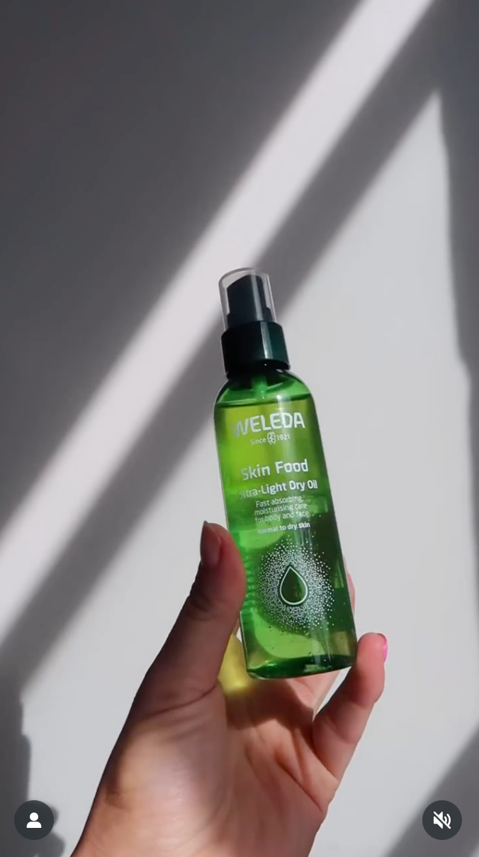 Rachael Ferguson Hand holding green Weleda skin food spray bottle with dramatic shadow lighting.