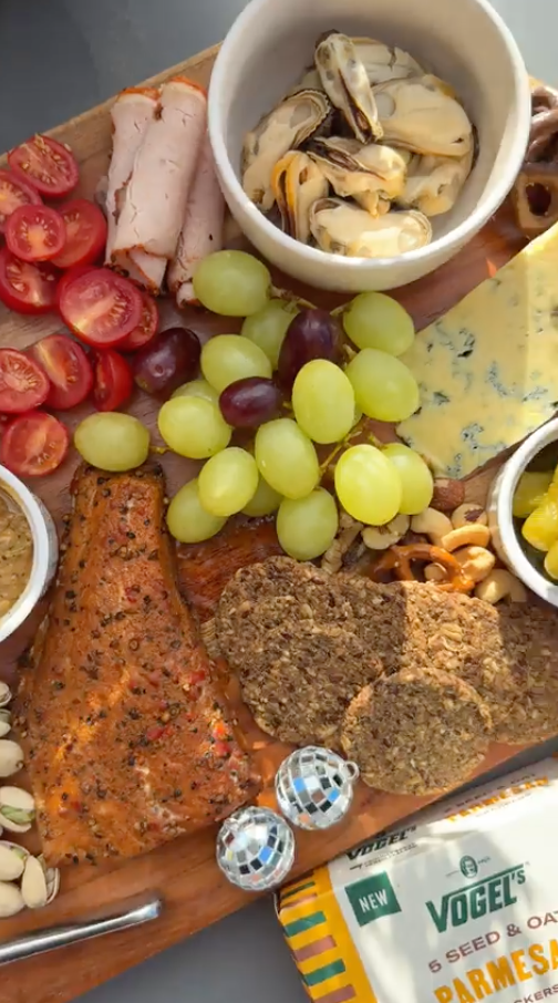 rachael ferguson content creator Charcuterie board with grapes, tomatoes, cheese, and bread arranged on wooden serving platter.