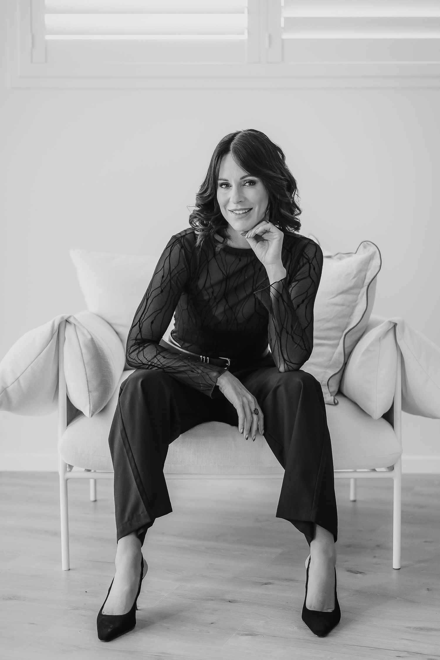 Black and white portrait of rachael ferguson content creator seated on a white couch wearing an elegant black outfit and heels.