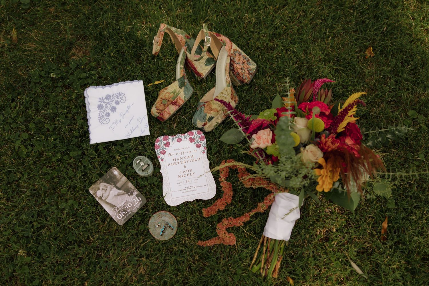 Wedding flat lay on grass featuring colorful bridal bouquet, invitation suite, ribbons, and accessories.