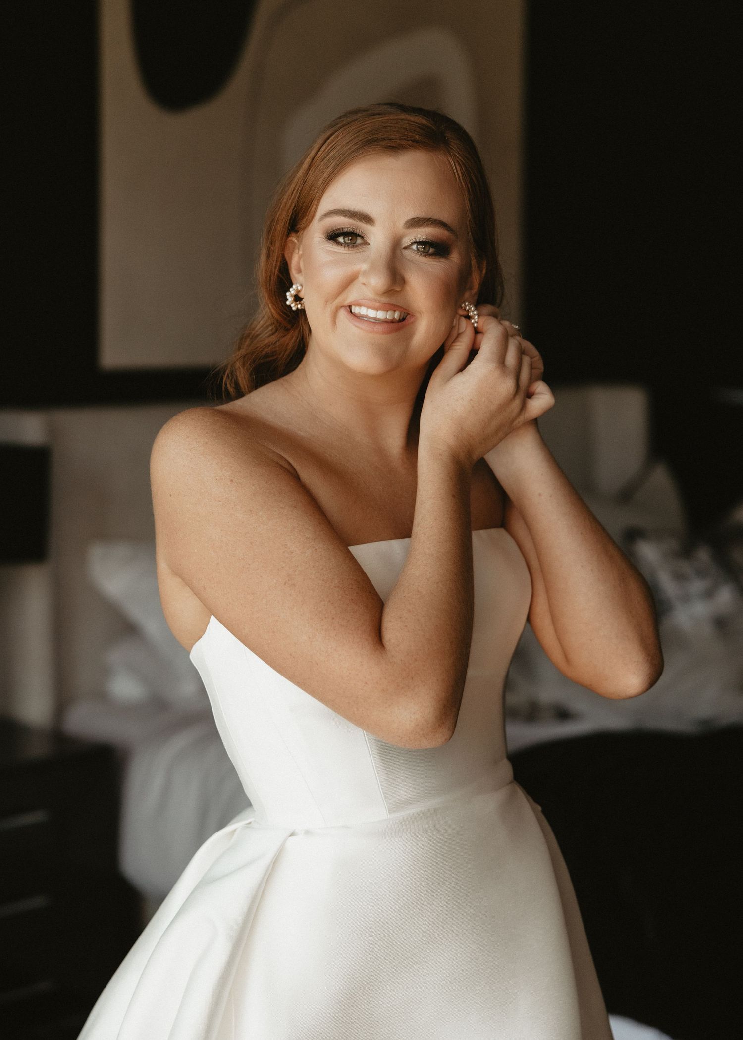 An elegant bridal portrait captured in natural light against a dark wall.