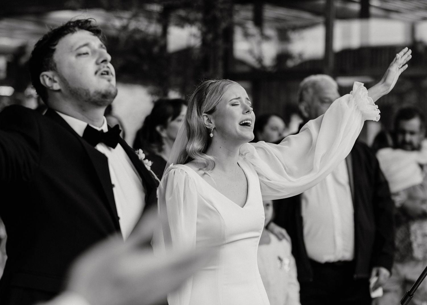Black and white photo of couple singing passionately with raised arms during wedding celebration.