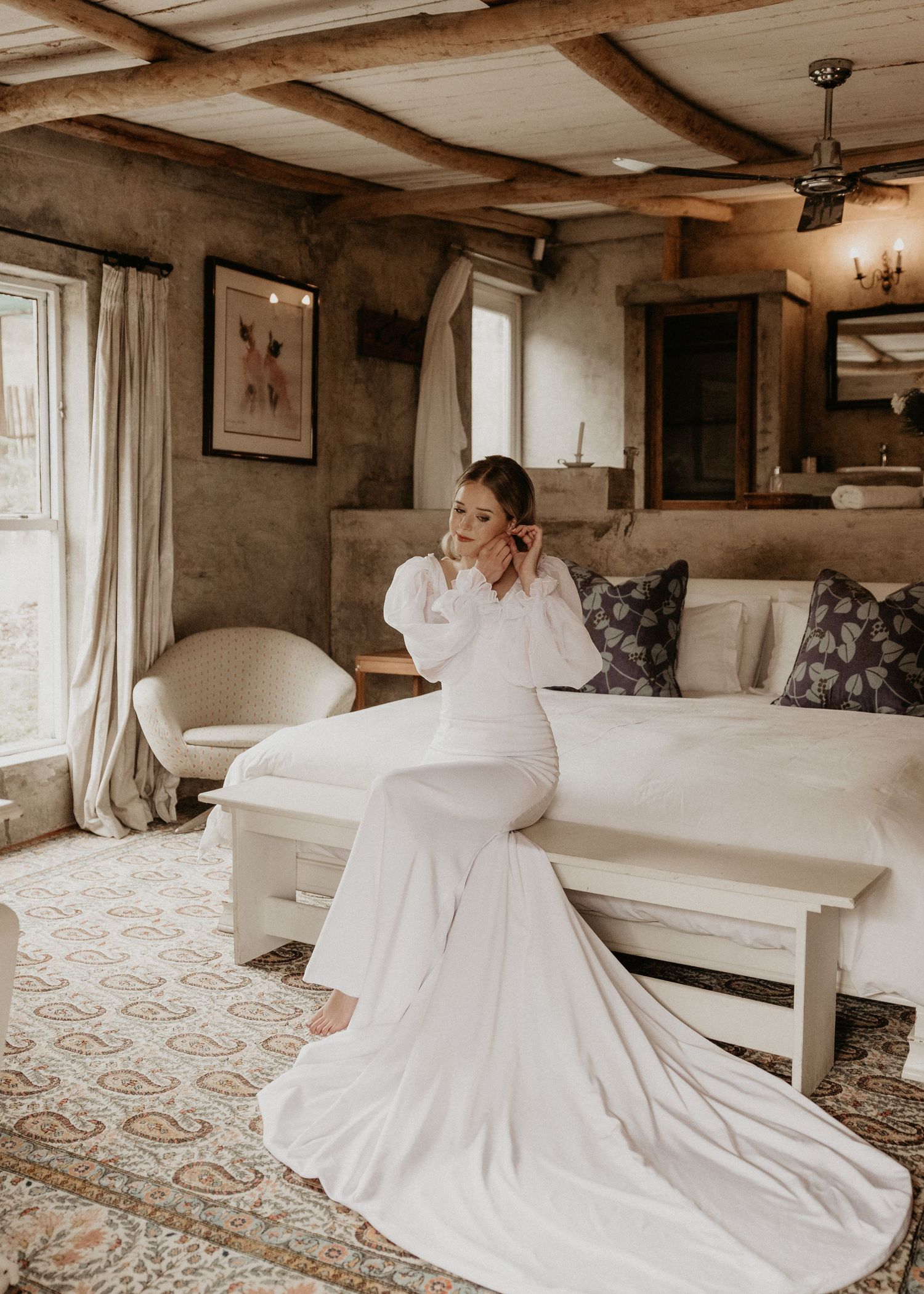 Elegant bridal portrait in a rustic room showing a flowing white dress train on a patterned rug.