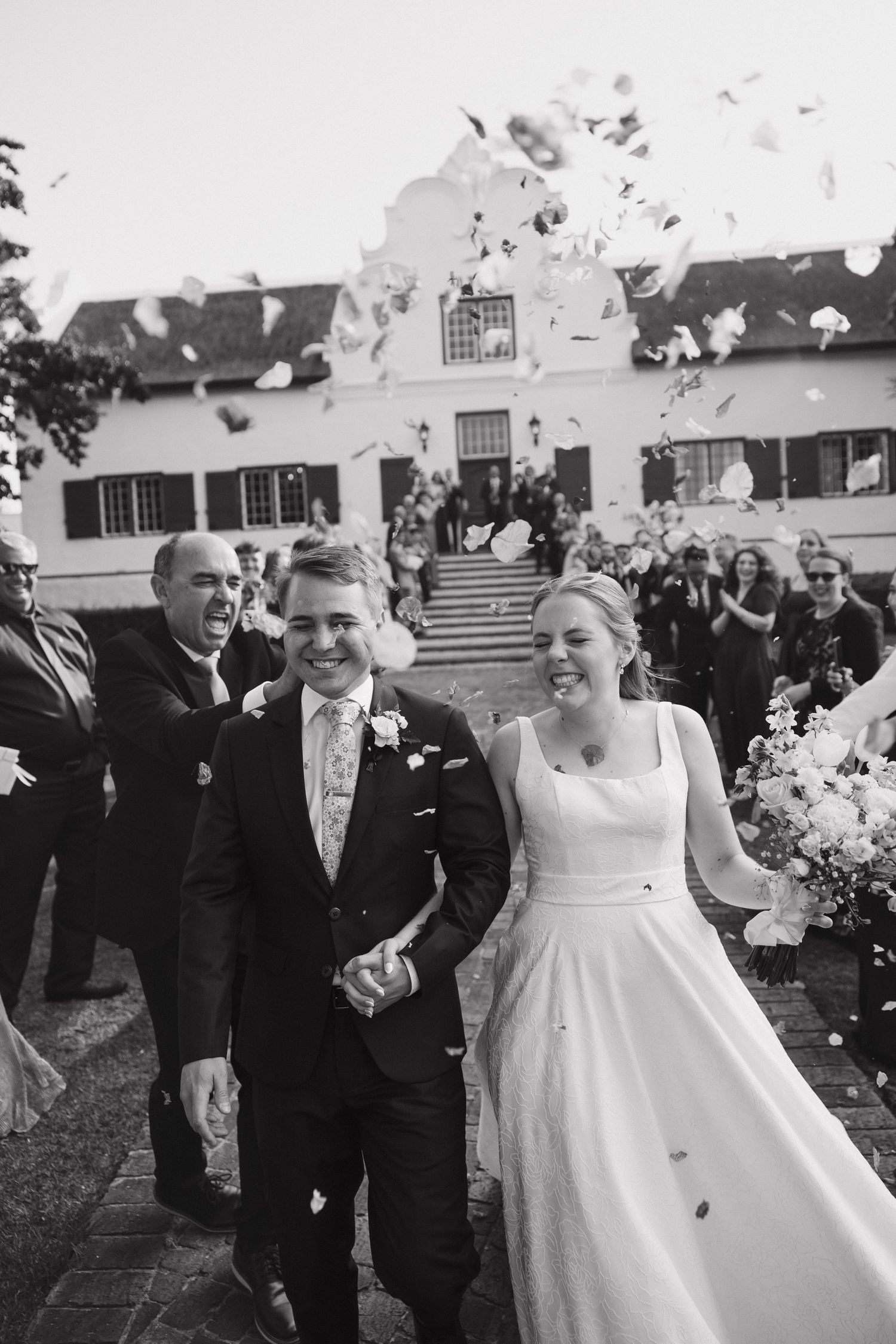 A joyful wedding celebration with confetti being thrown over a bride in a white dress at an outdoor venue.