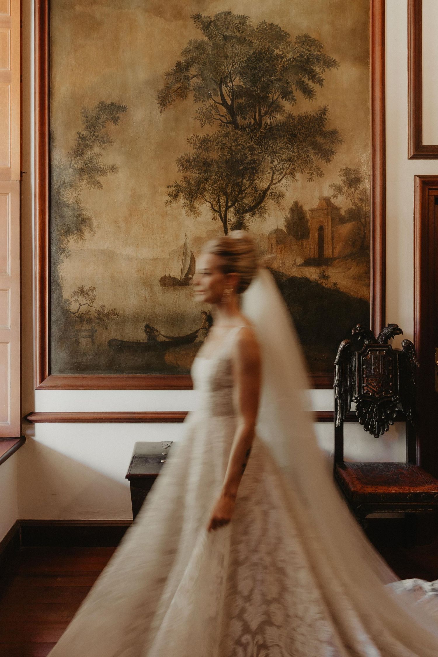 Motion blur captures ethereal bridal figures in white gowns against vintage landscape wall paintings in an elegant room.