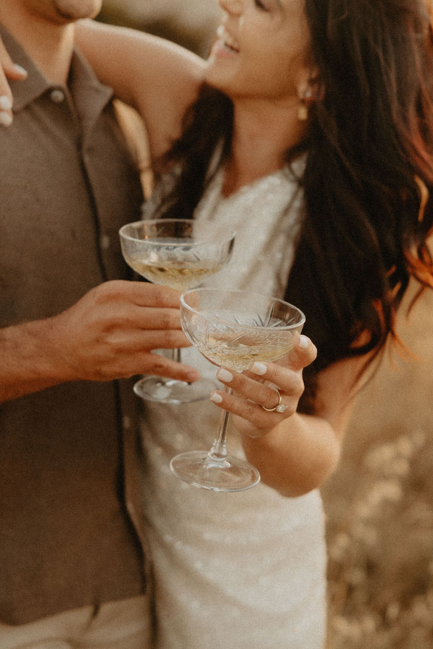 A couple toasts with vintage champagne coupe glasses at golden hour, creating a romantic atmosphere.