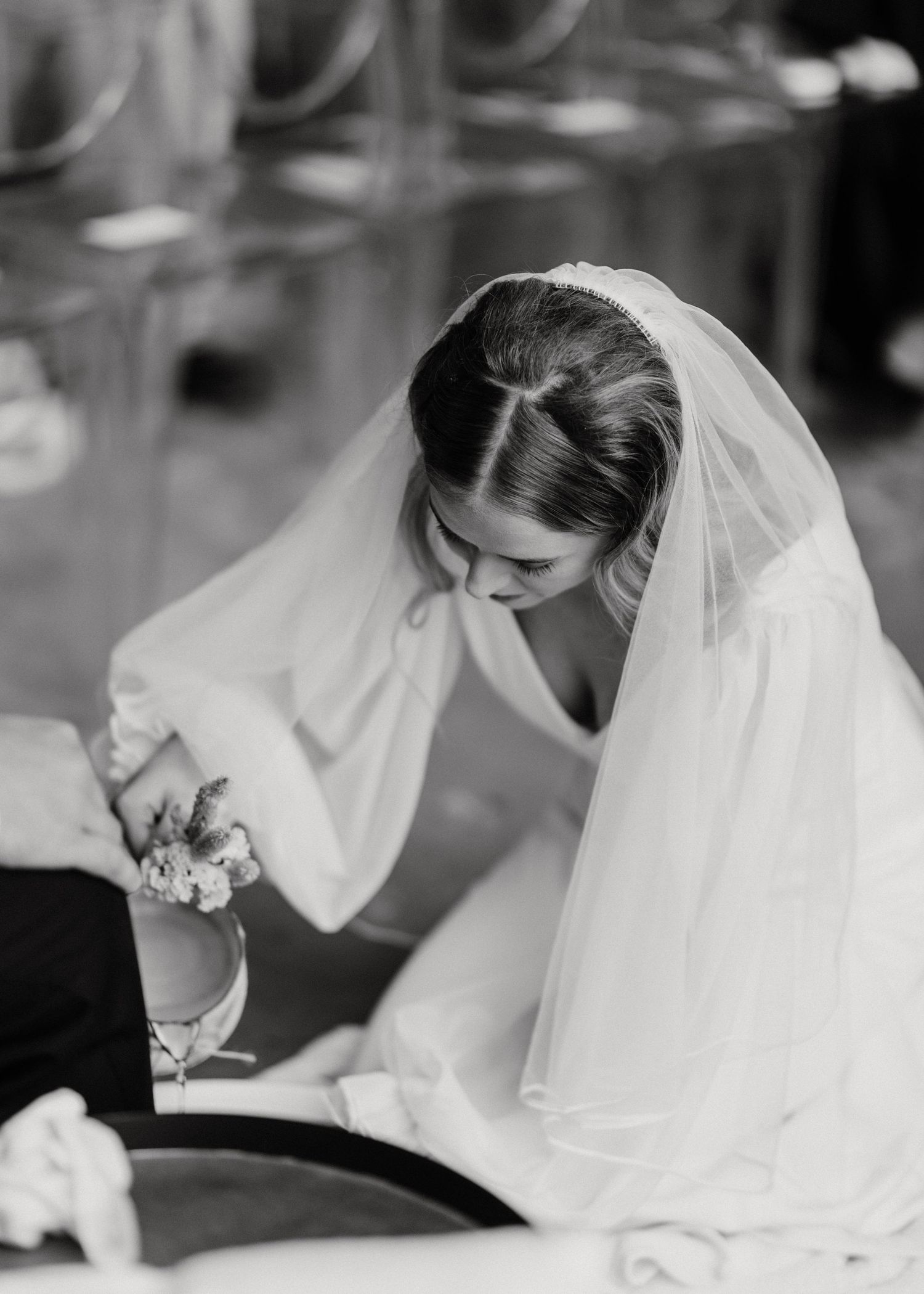 A bride in flowing white dress and veil bends down performing a wedding ritual.