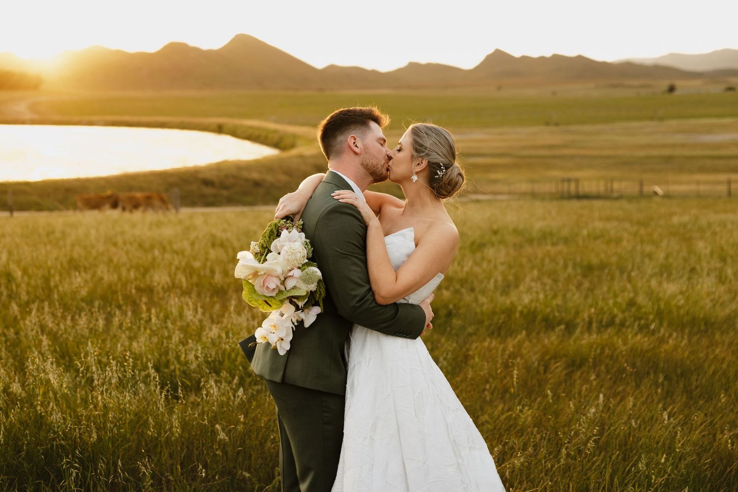 A couple shares a romantic kiss in a golden wheat field at sunset during their wedding photoshoot.