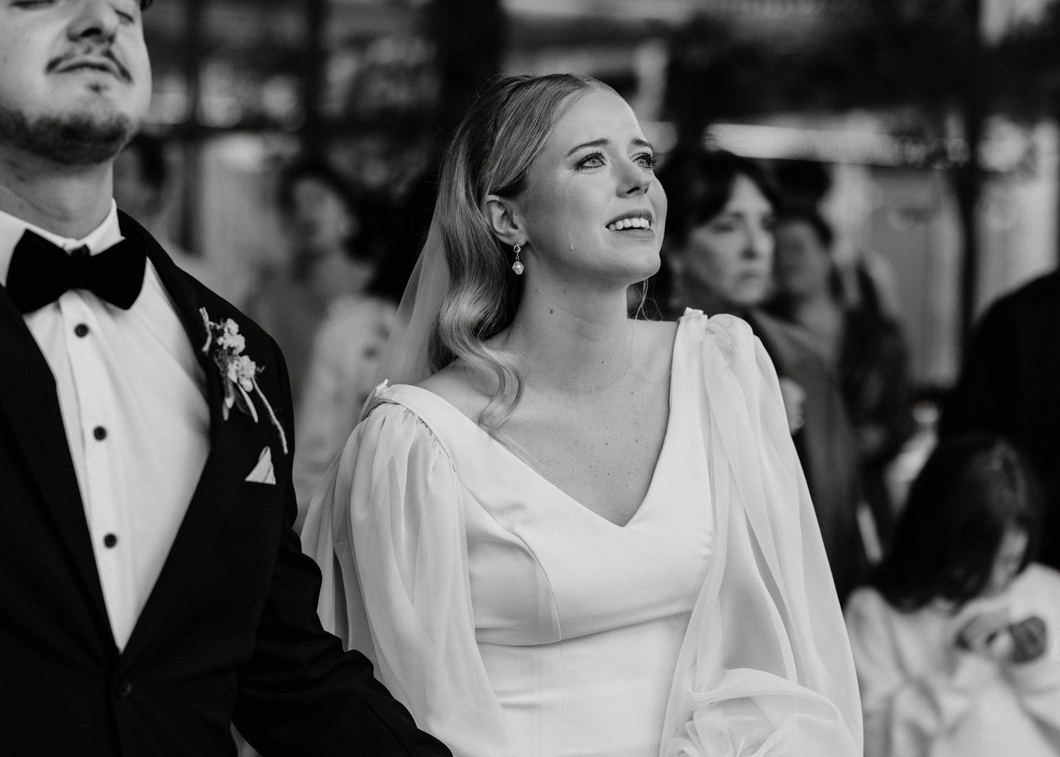Elegant bride in white v-neck dress with bishop sleeves smiles during wedding ceremony.