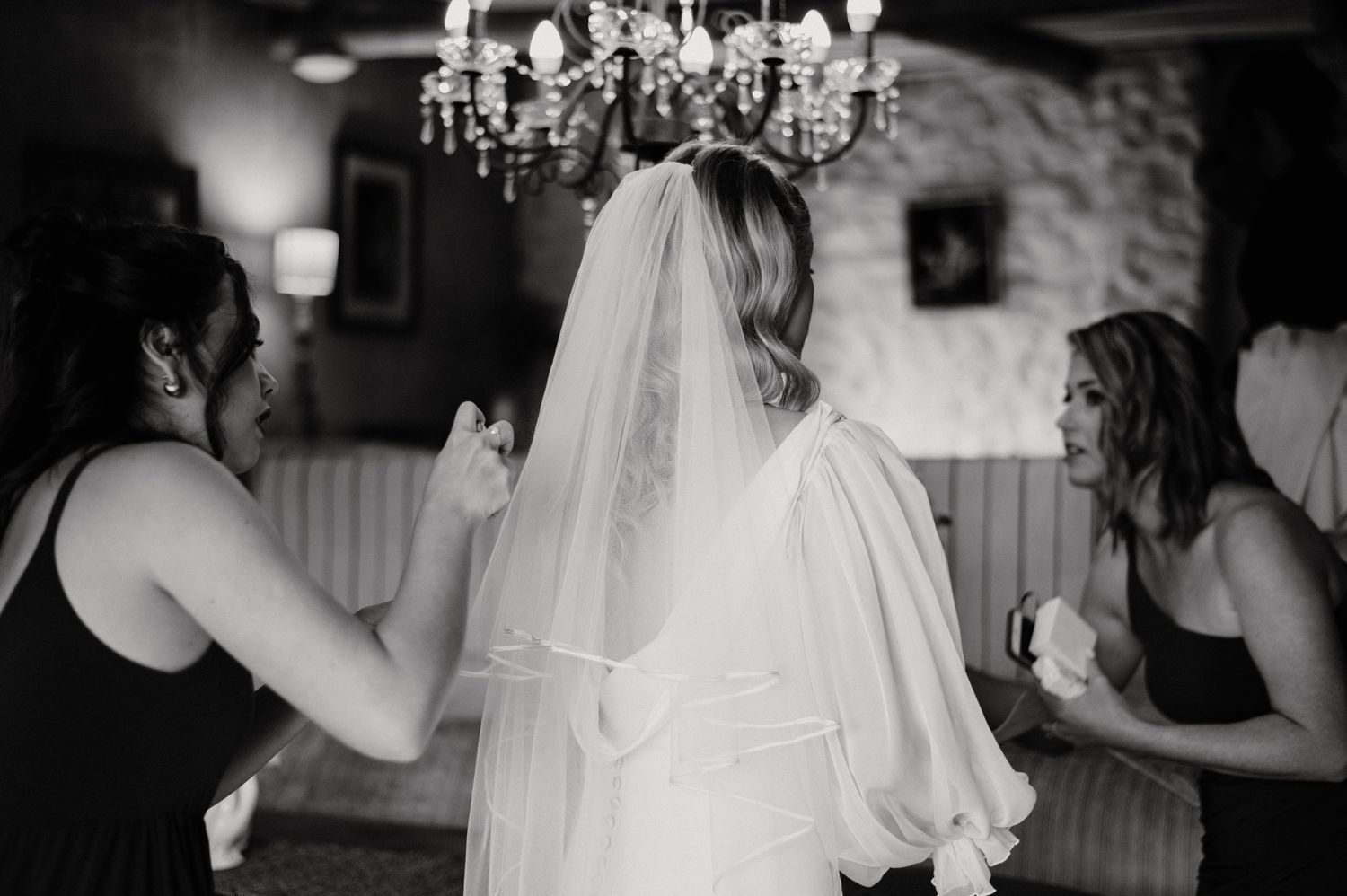 Black and white photo of wedding preparation moment under crystal chandelier.