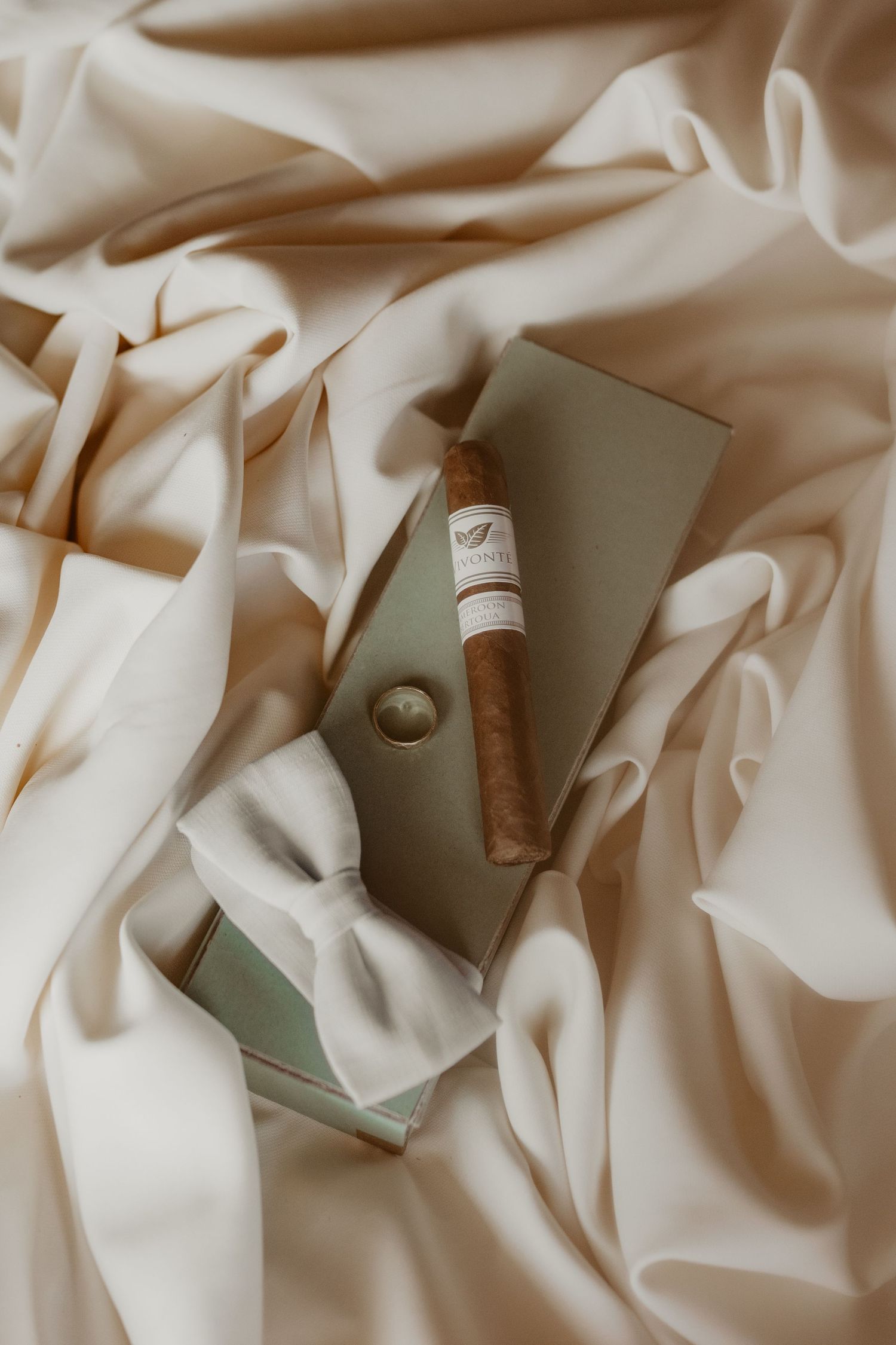 A cigar and notebook arranged on soft cream-colored fabric with elegant folds creating a luxurious still life composition.