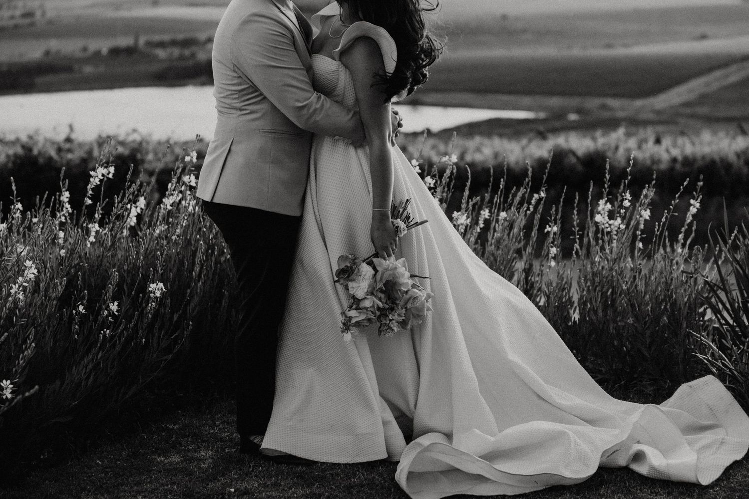 Couple shares romantic moment at sunset in a golden field with mountains in background.