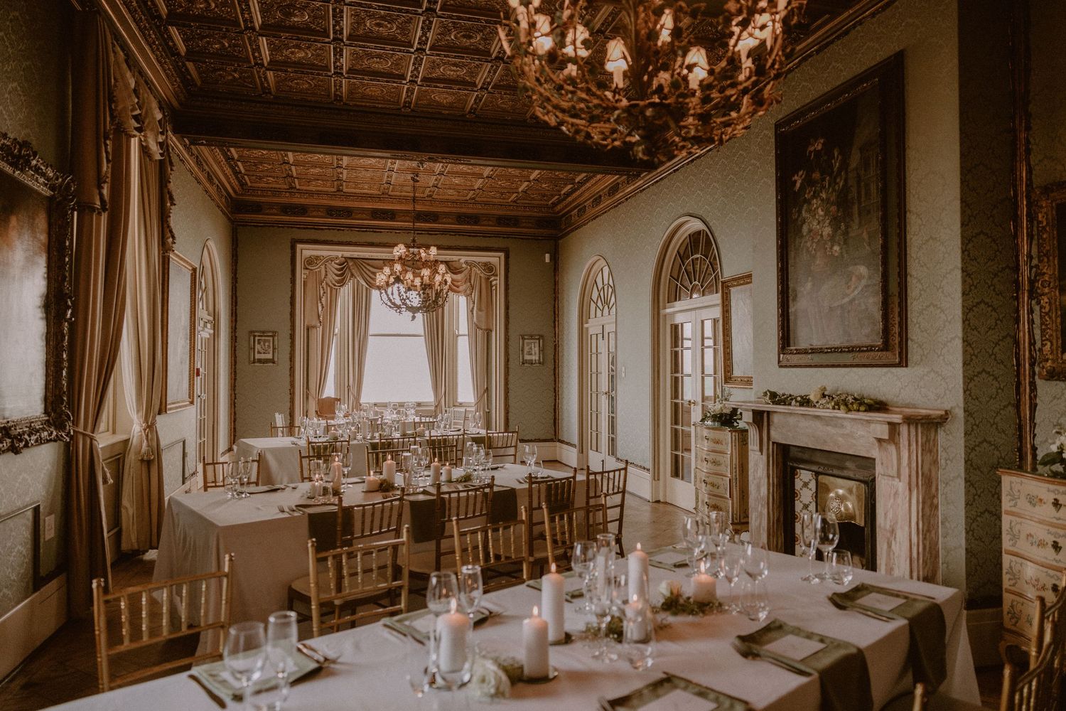Elegant wedding reception dining room with chandelier, fireplace and formal place settings.
