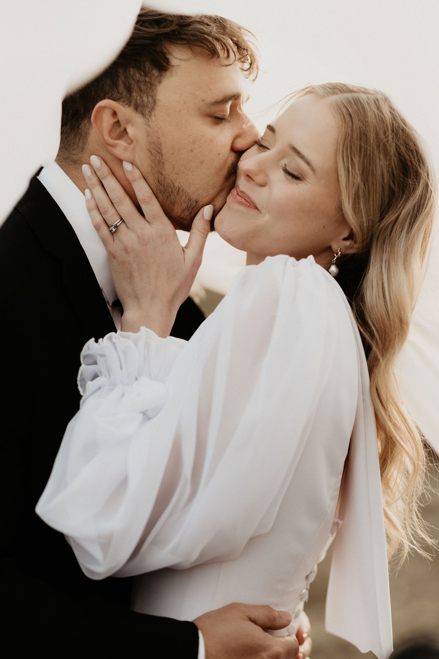 Romantic wedding portrait showing a tender kiss with the bride in puff-sleeve dress and groom in classic tuxedo.