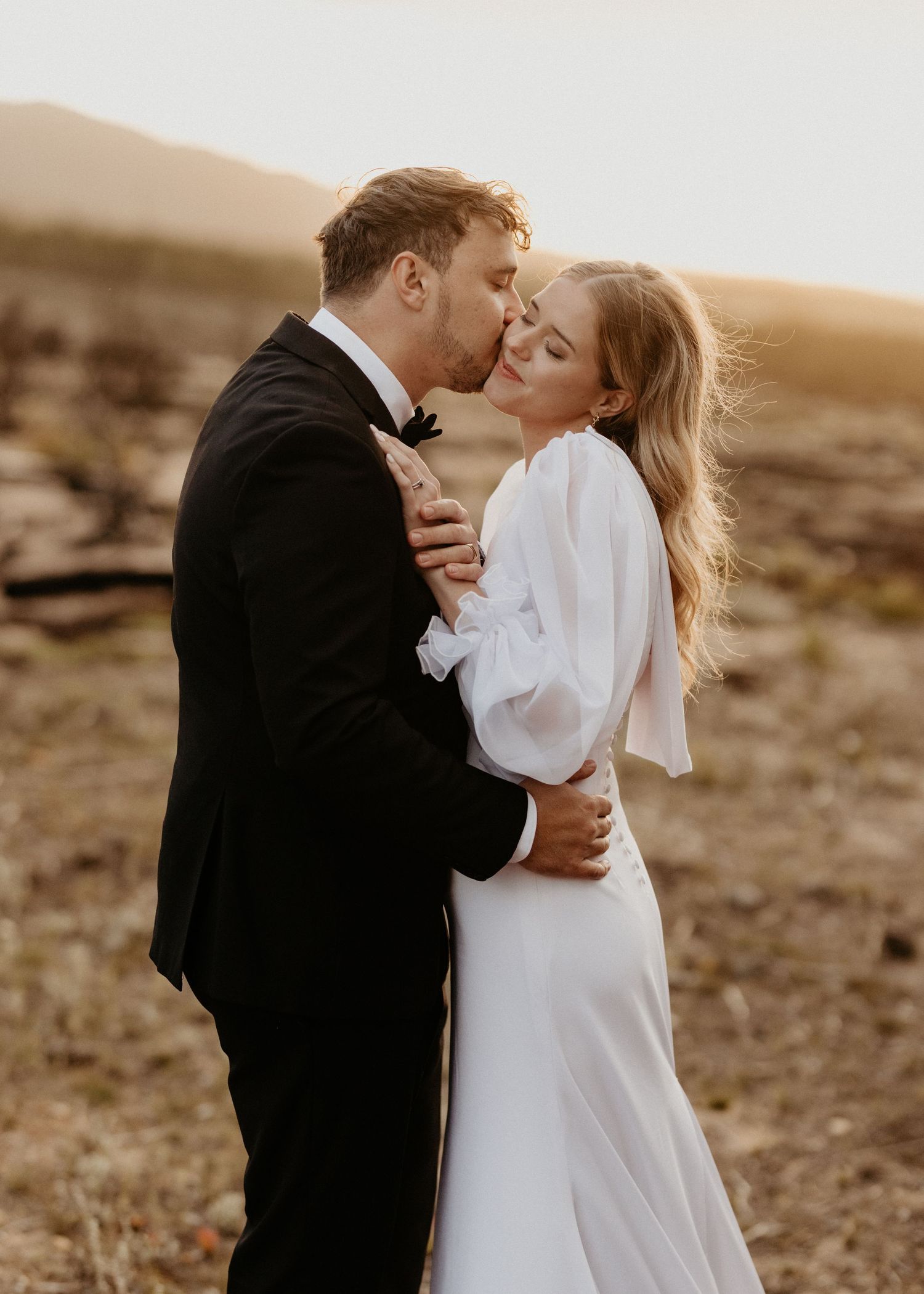 Wedding couple shares intimate moment during golden hour desert photoshoot.