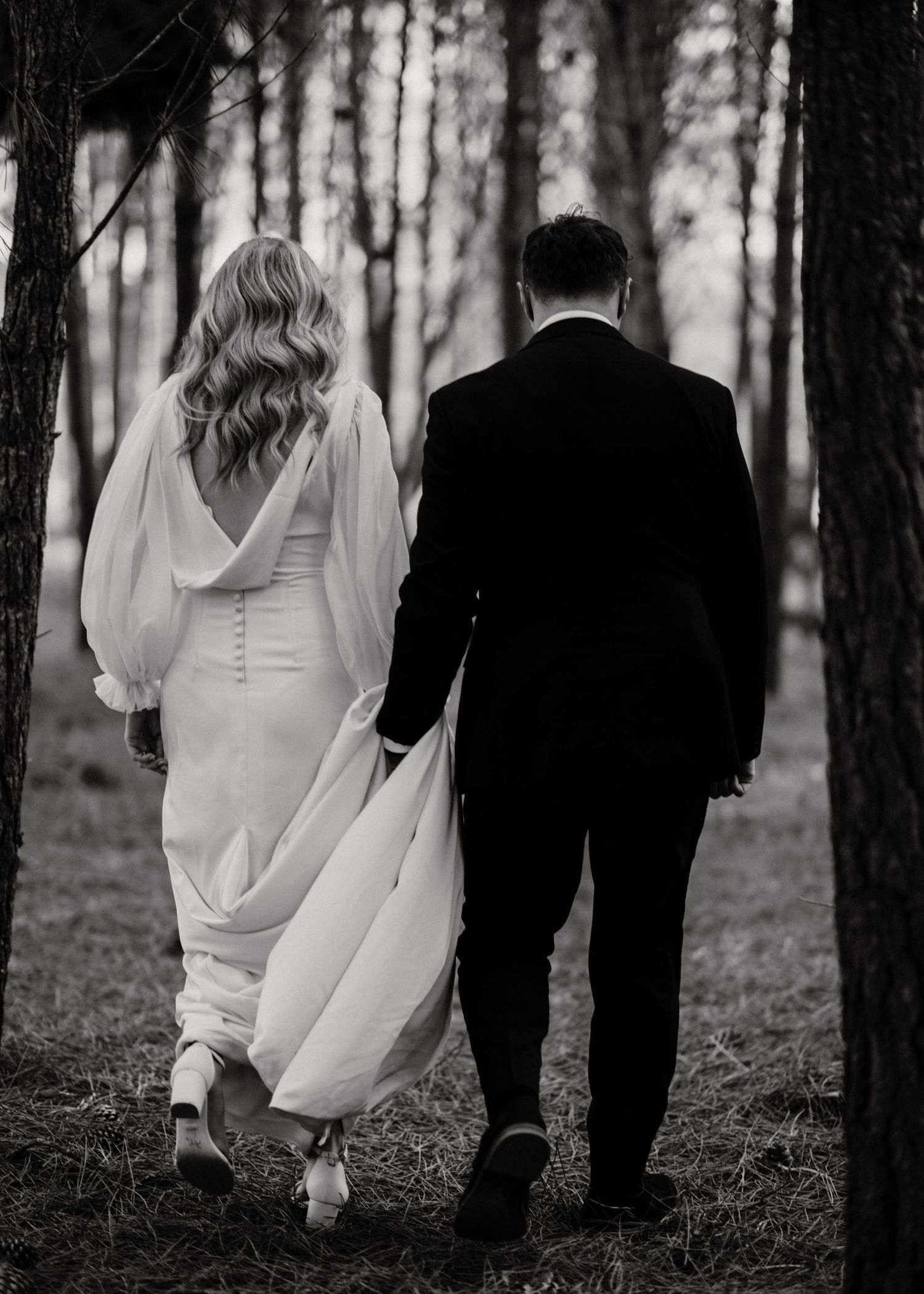 Black and white photos of couple walking through pine forest in wedding attire.