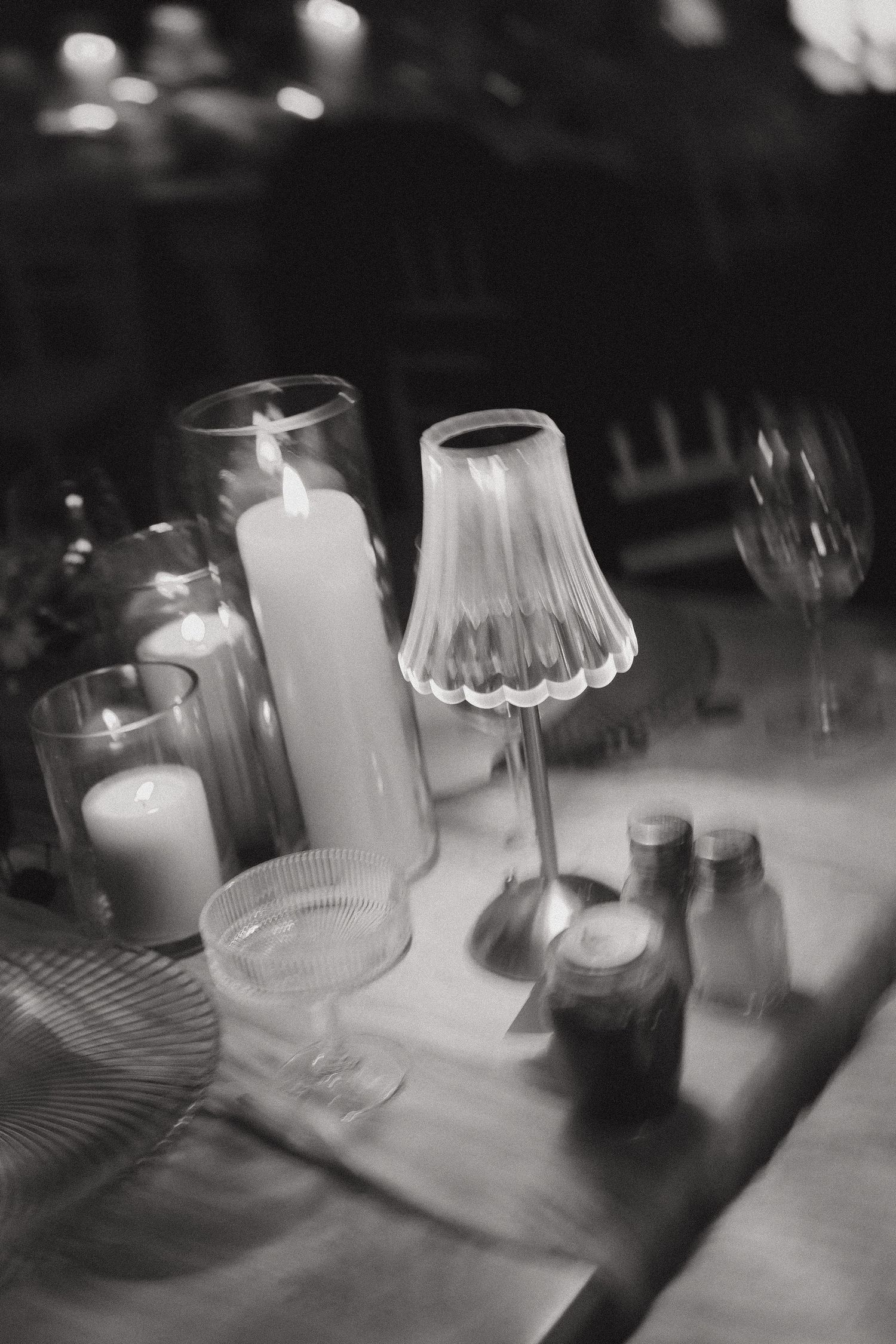 Black and white photo of elegant table setting with lit candles, glass lamp, wine glass, and salt shakers.