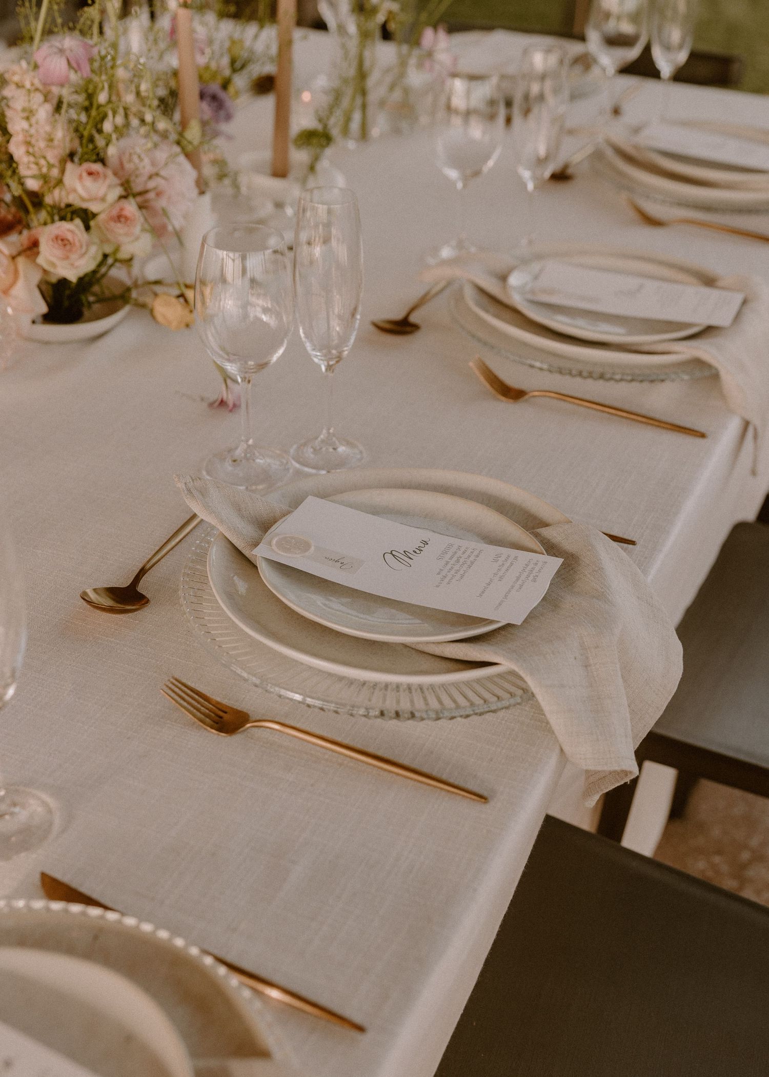 Romantic wedding table setting with blush flowers and gold flatware.
