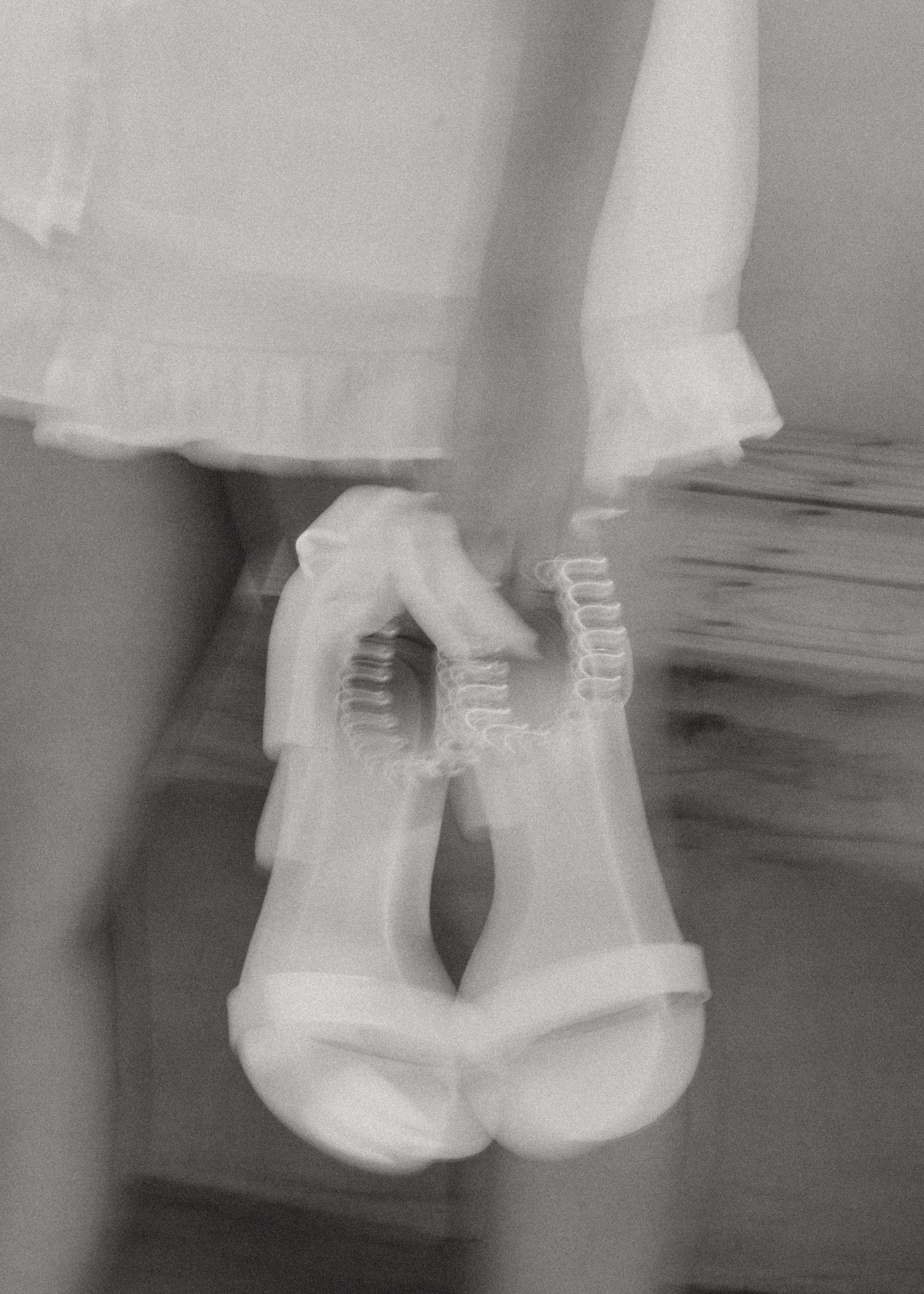 Black and white image of feet in clear shoes dangling above wooden floor.