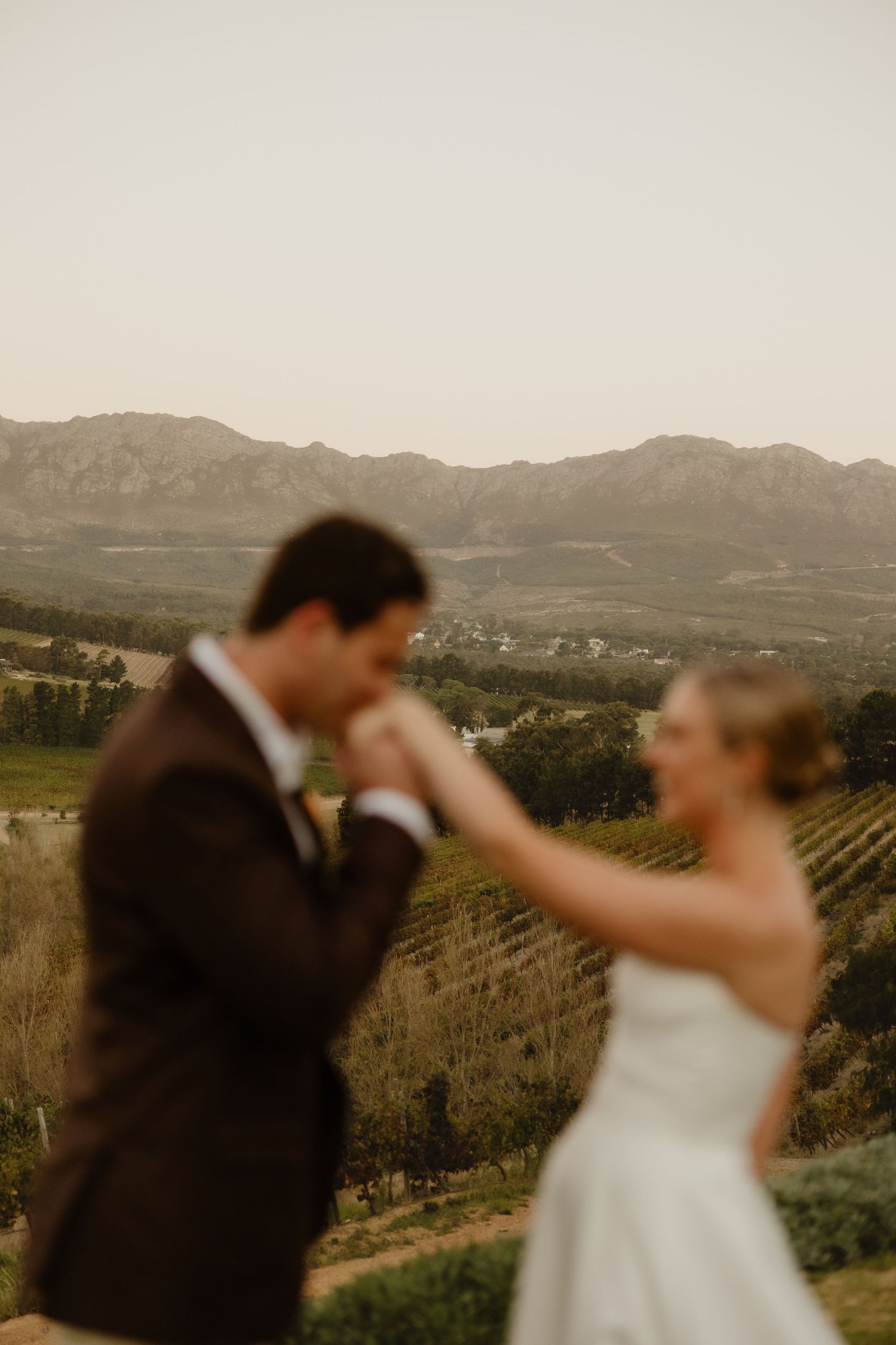 A bride and groom share a romantic dance with scenic vineyard and mountain views in the background.