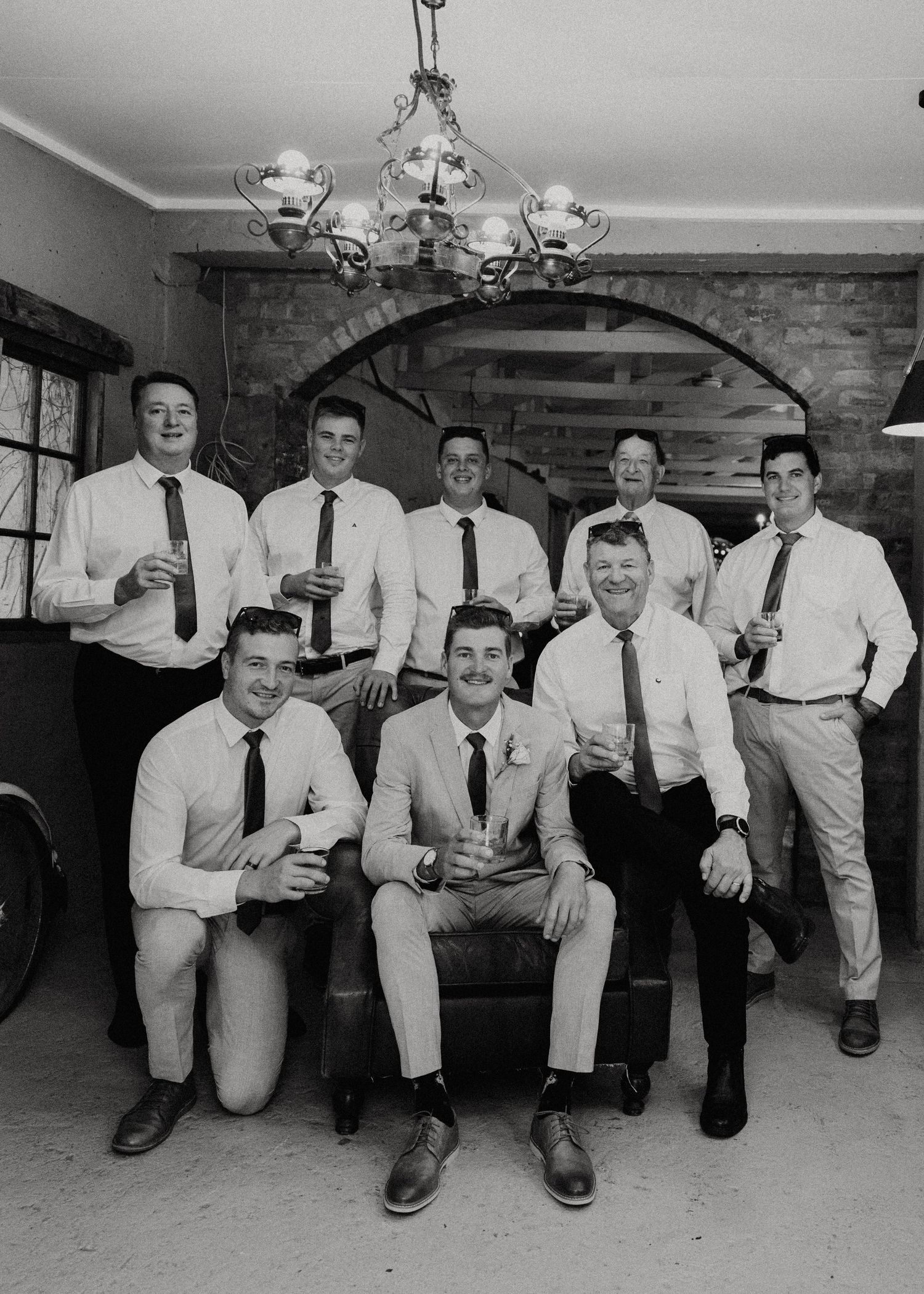 Wedding party in formal attire sitting together on a bench in black and white photography.