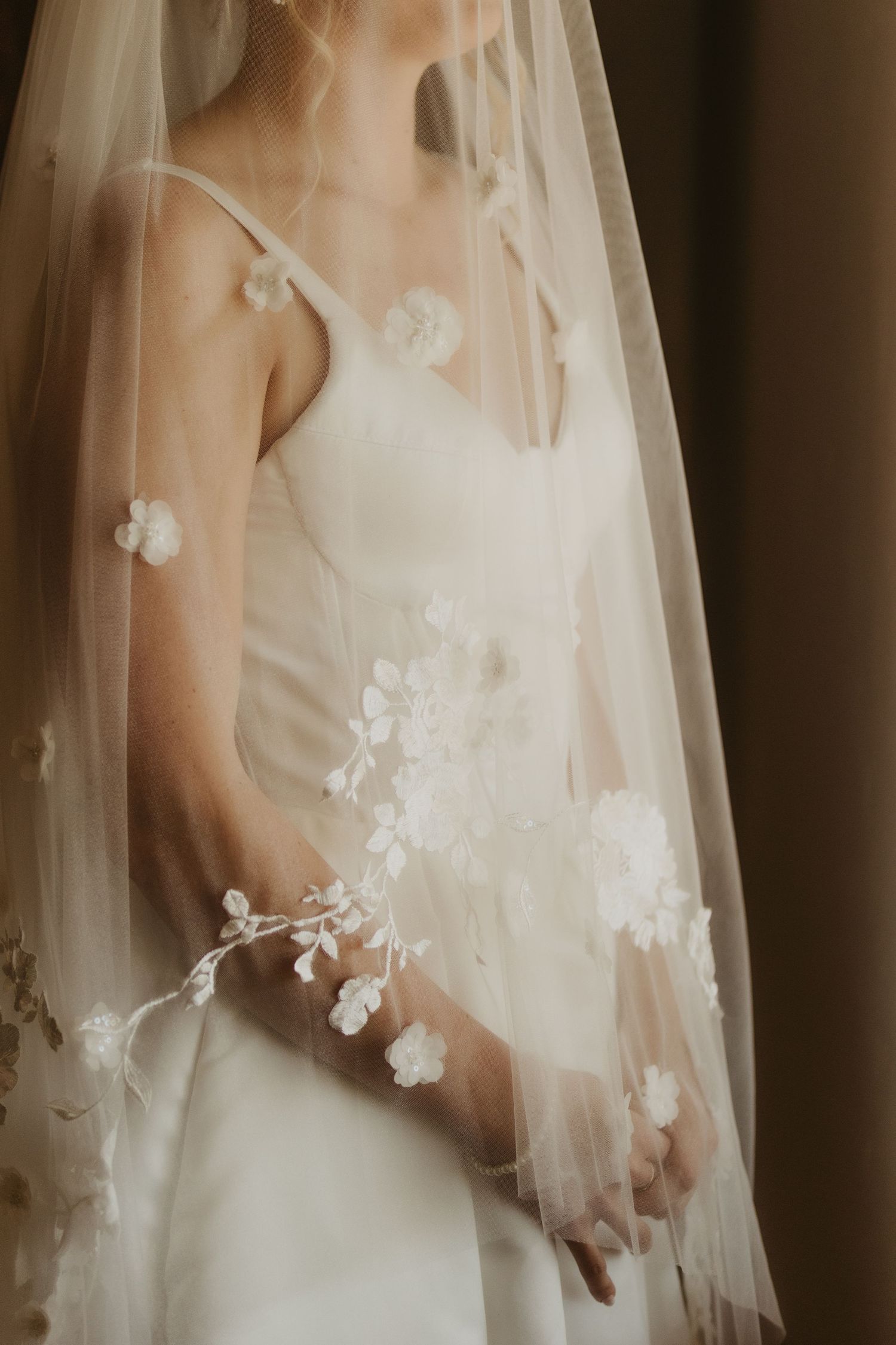 Close-up details of delicate floral appliques on a romantic sheer tulle wedding veil against a soft cream background.