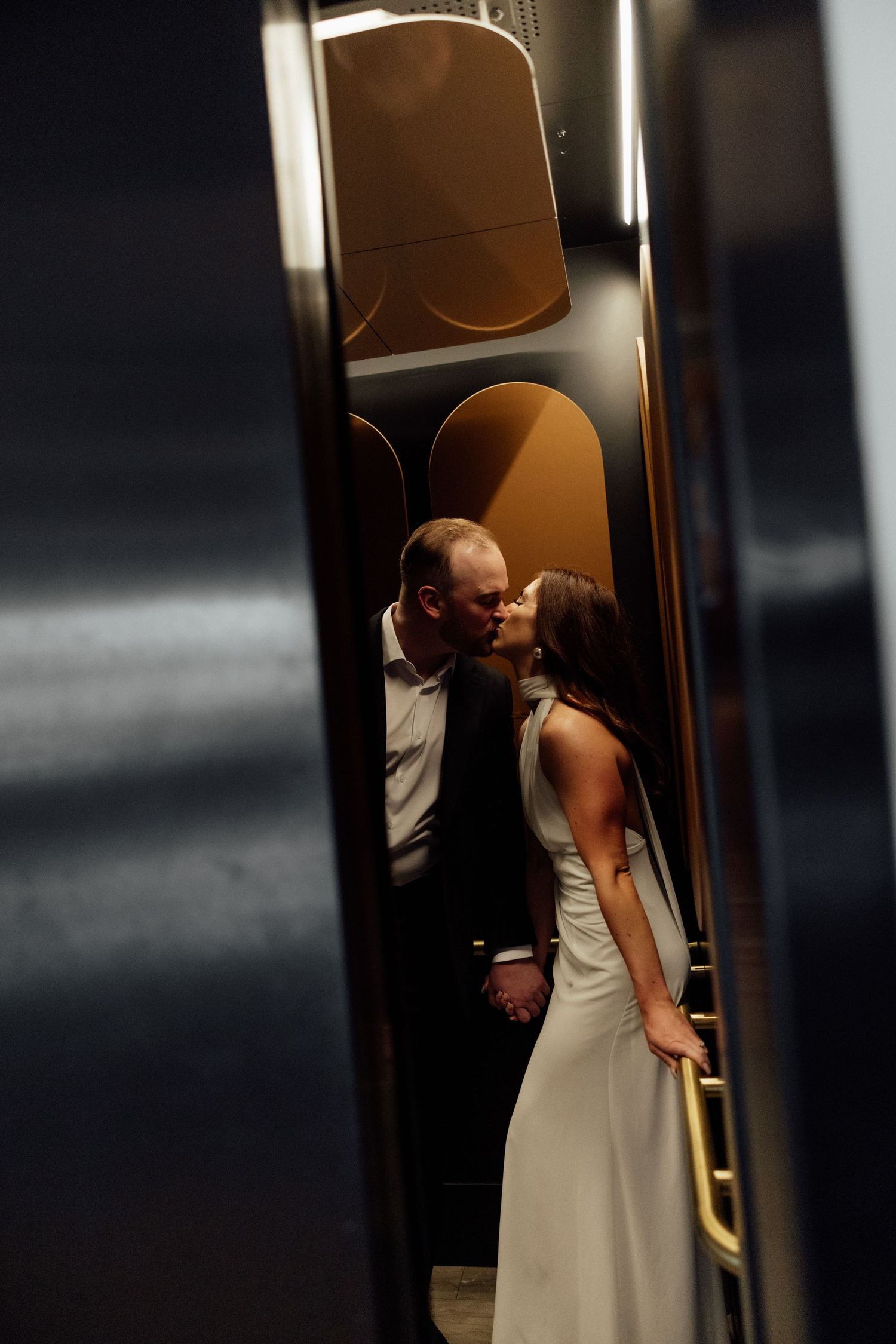Two figures in formal attire share an intimate moment inside an elevator.
