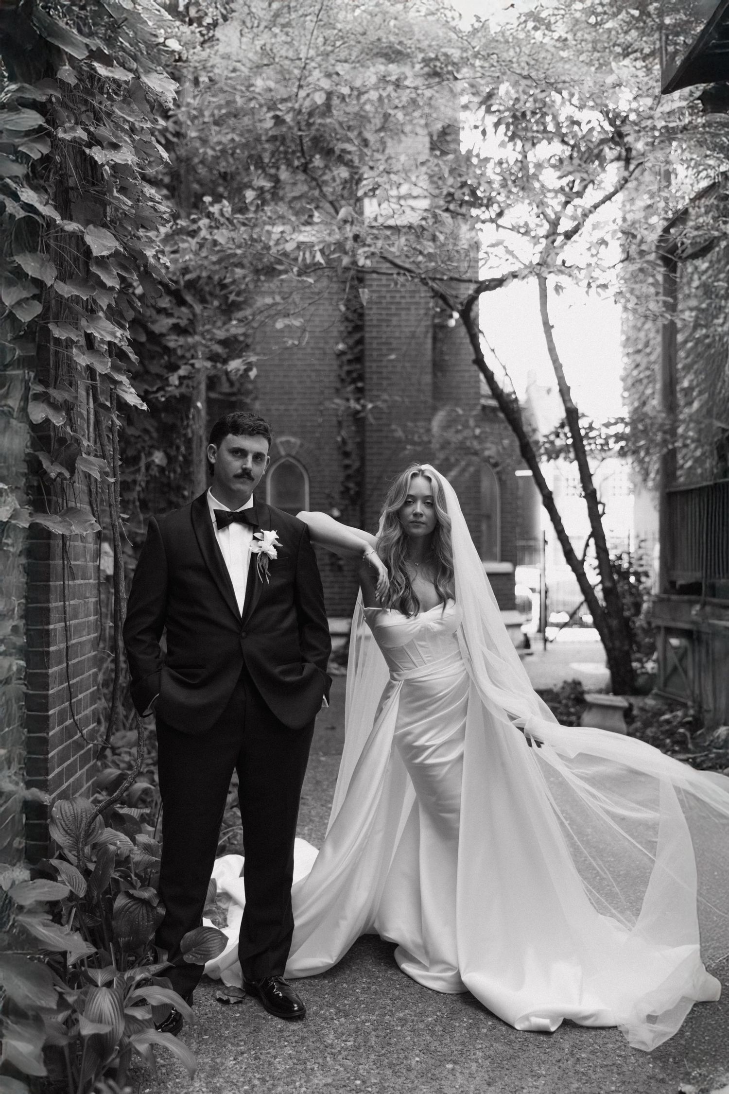 A black and white photo series showing a romantic wedding couple walking through a garden path with stone walls.
