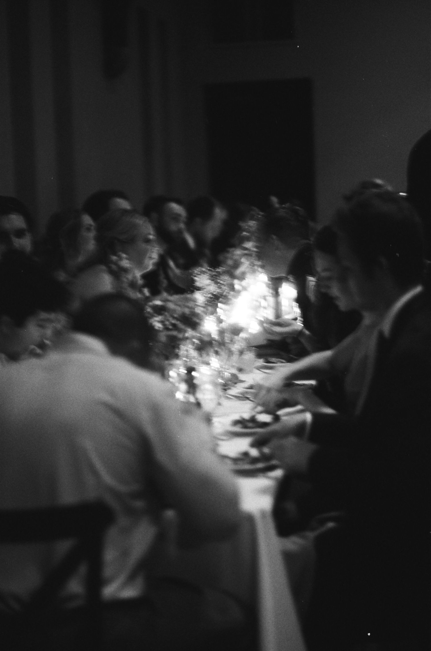 A dimly lit reception dinner table with guests gathered around candlelight.