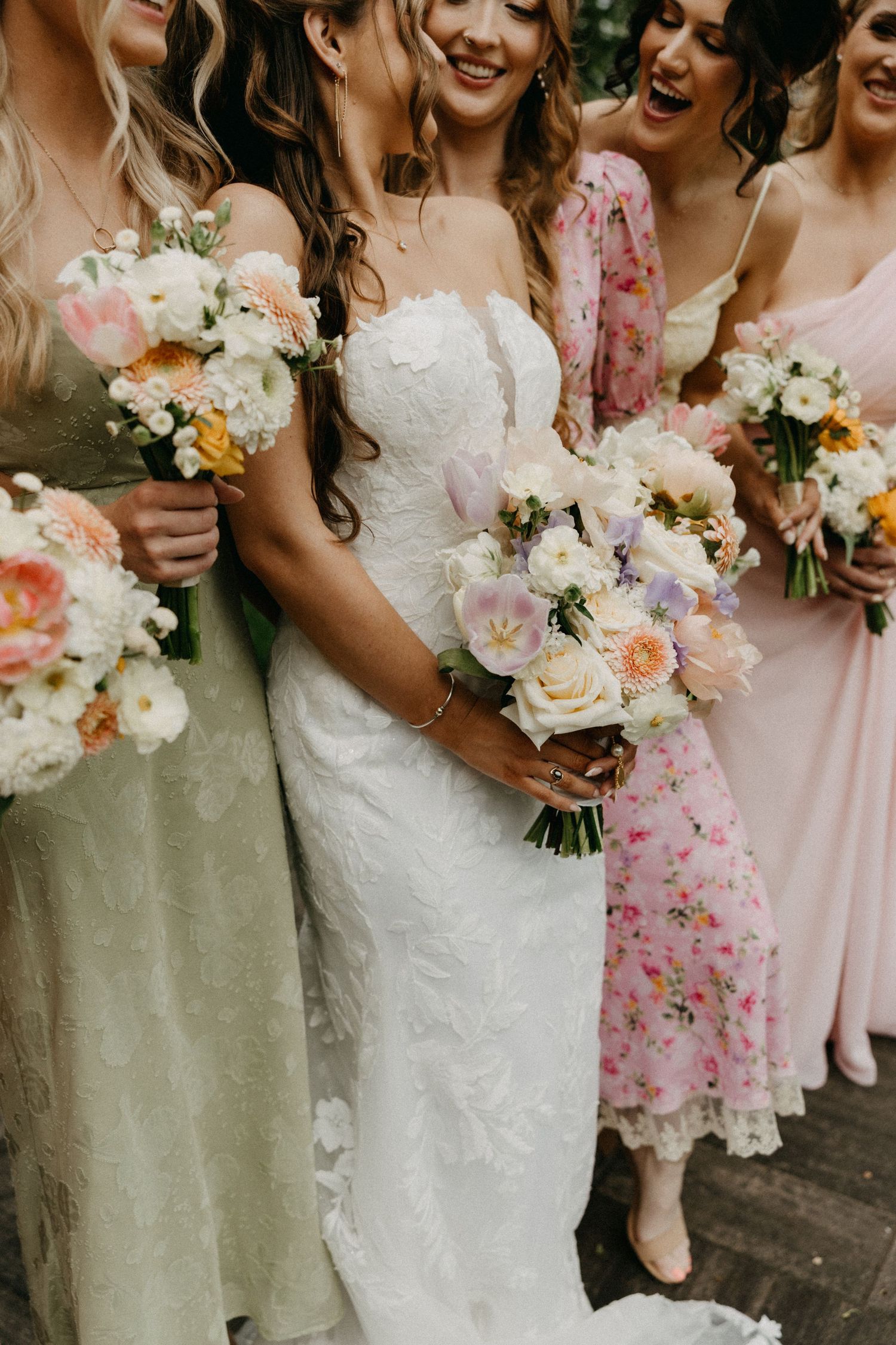 Bridesmaids in pastel dresses holding beautiful bouquets of pink and white flowers.