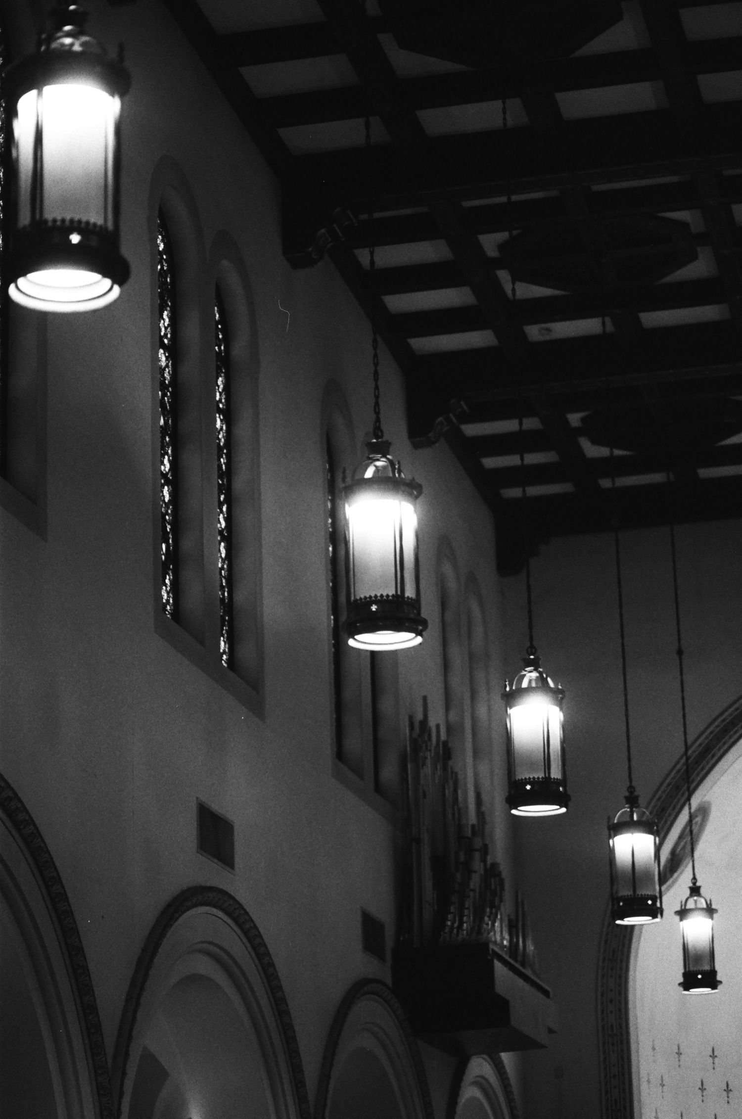 Gothic-style church interior with hanging lanterns and stained glass windows in black and white.