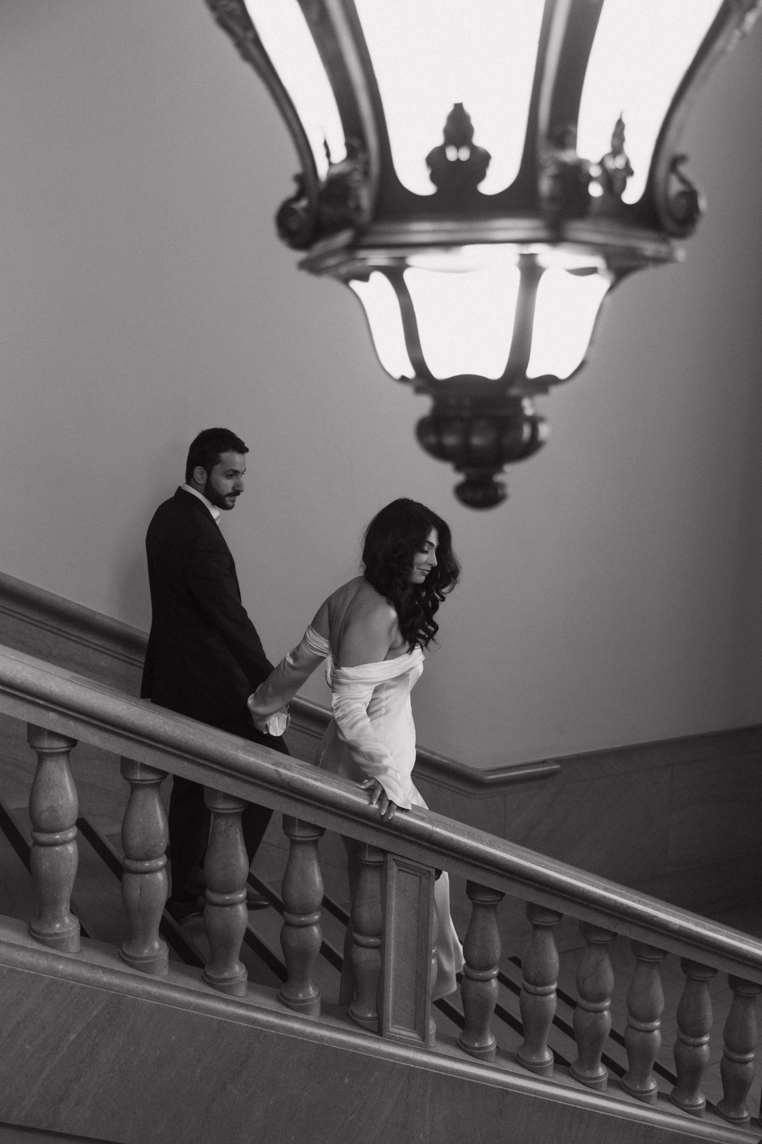 Couple ascending grand staircase under vintage lamp lighting.