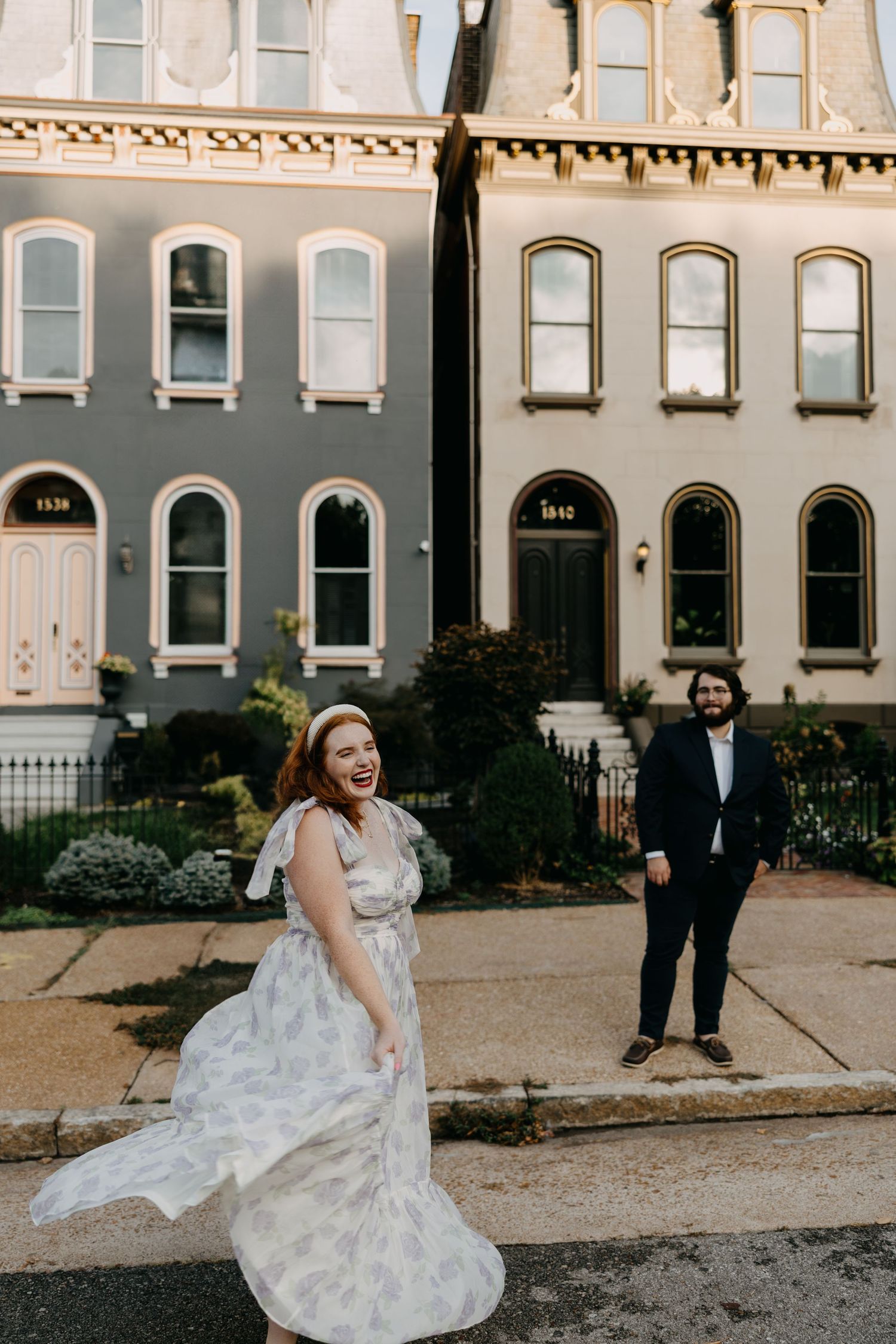 A couple in wedding attire poses outside historic brownstone buildings on a city sidewalk at sunset.