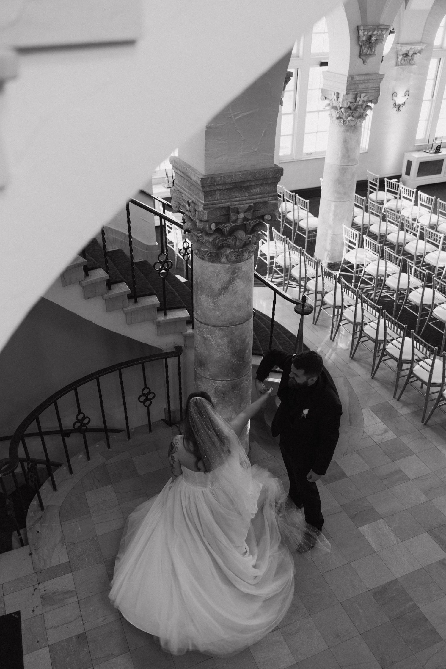 A black and white photograph capturing a wedding moment on a grand staircase with classical architecture.