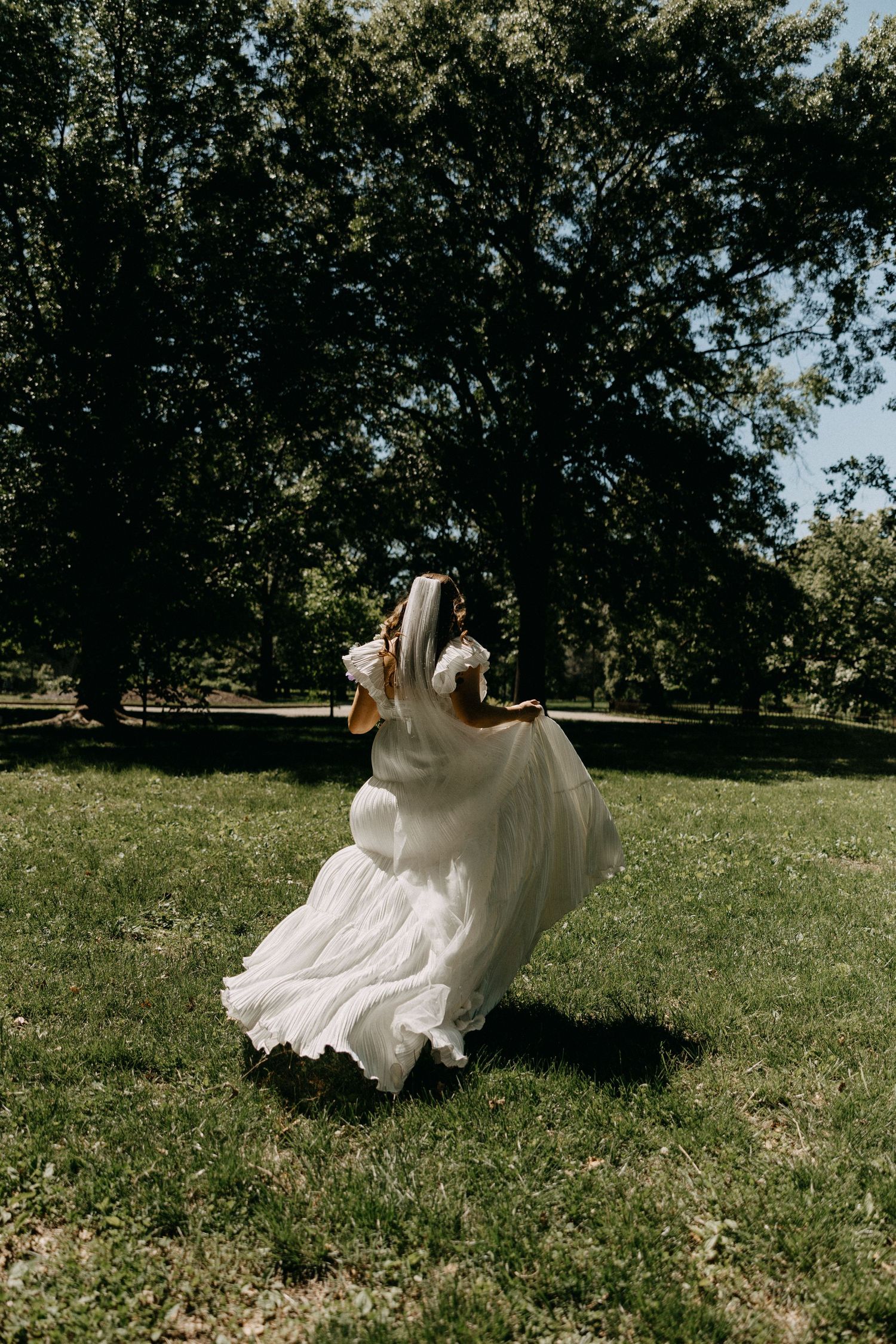 A flowing white wedding dress twirling in motion against a backdrop of trees in a sunlit park.
