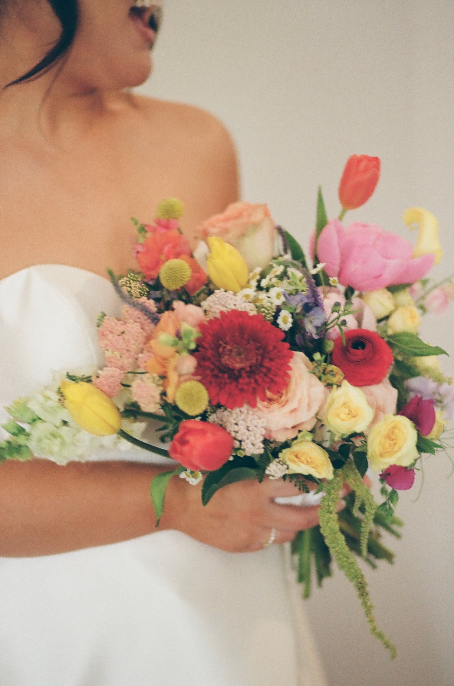 Vibrant wedding bouquet with colorful tulips, dahlias, and mixed flowers against white dress.