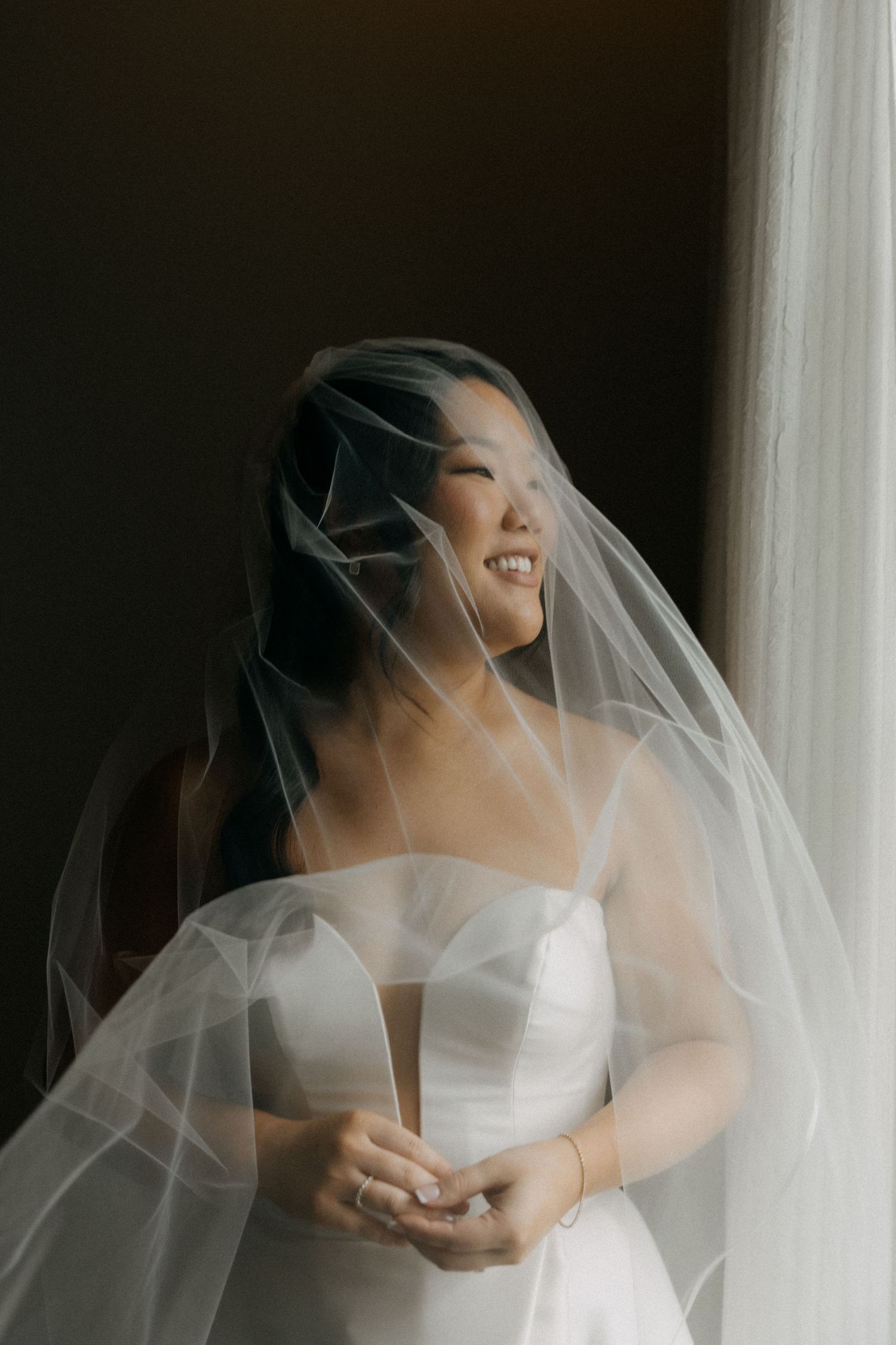 Artistic bridal portrait with soft veil movement against dark background.