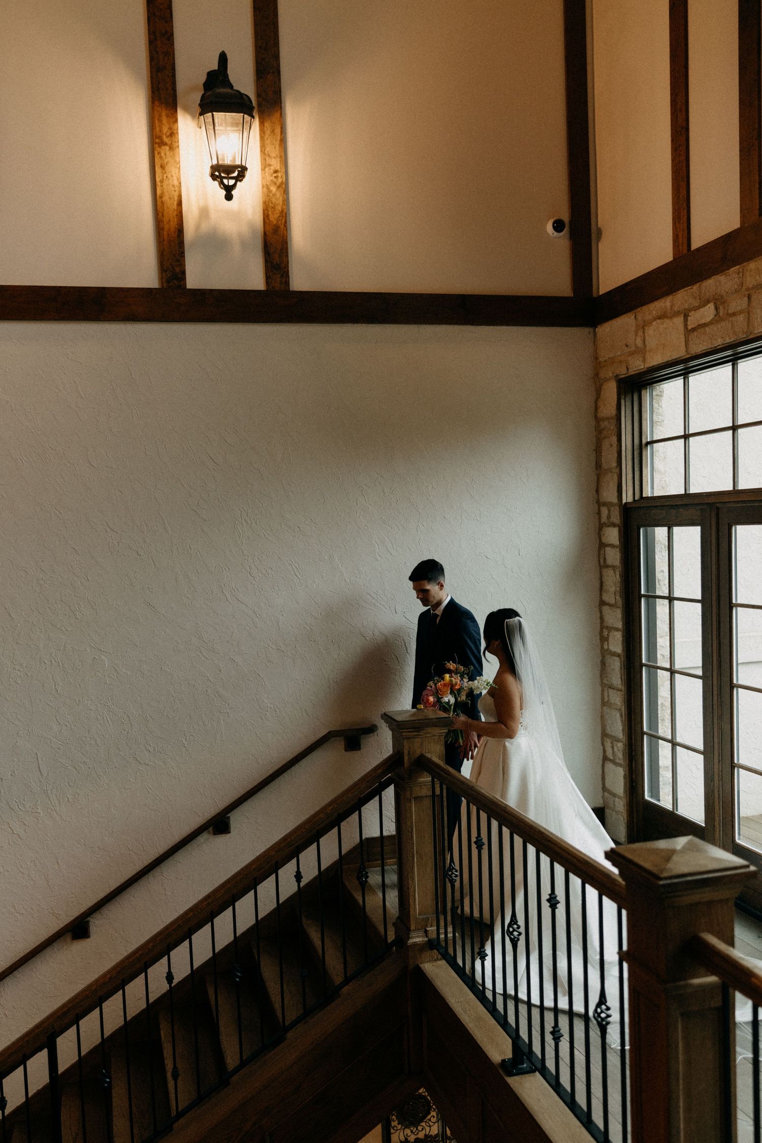 A couple shares an intimate moment on an elegant staircase landing with stone walls and vintage lighting.