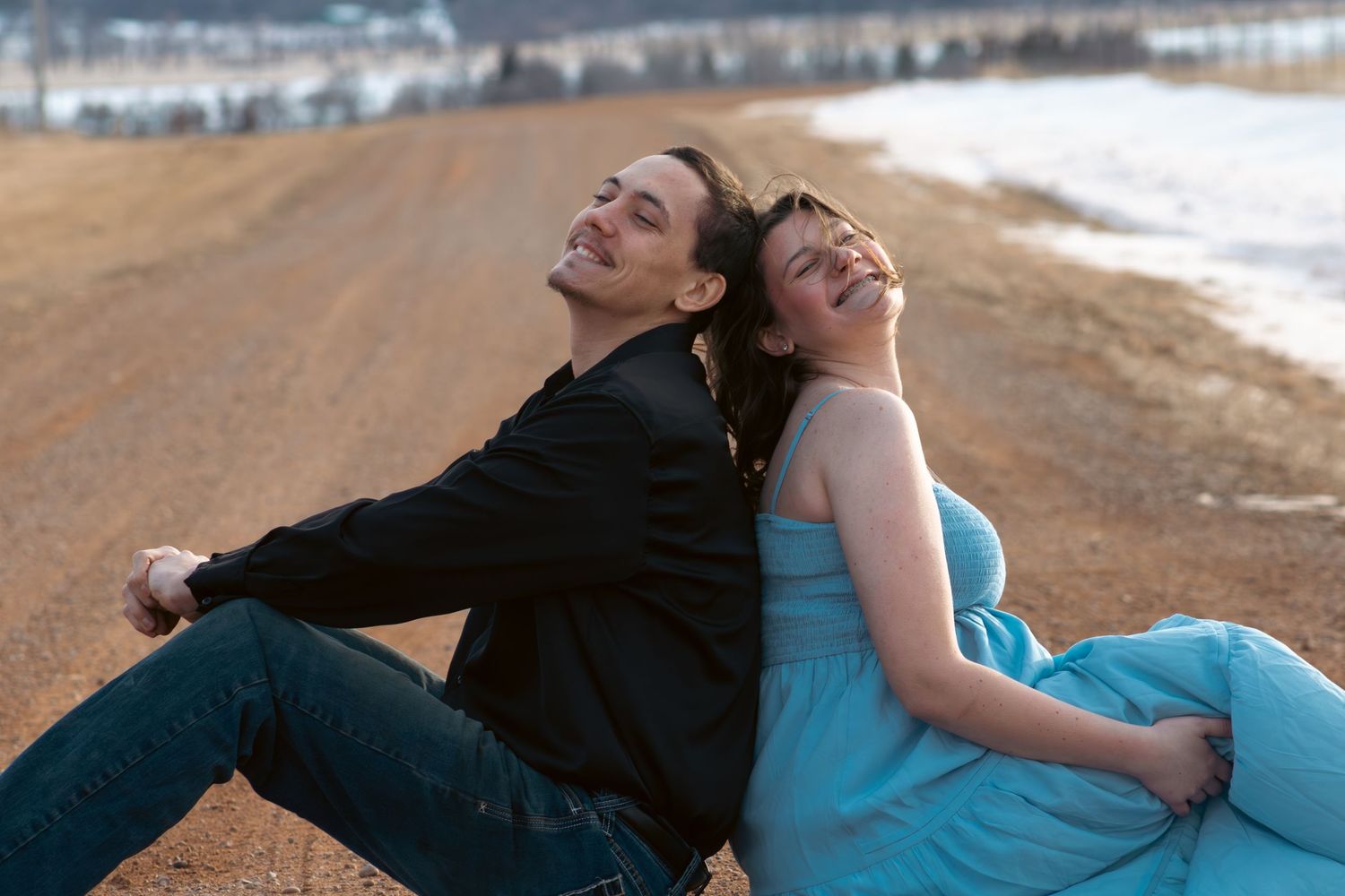 A couple in casual attire lies together on a sandy beach during sunset.