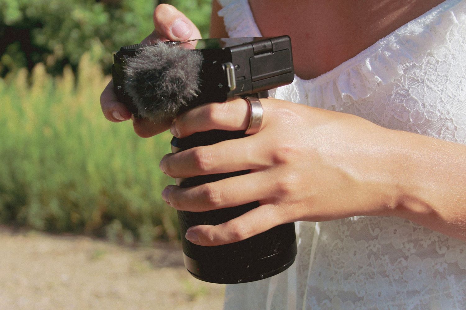 Close-up of hands holding and operating a digital camera outdoors.