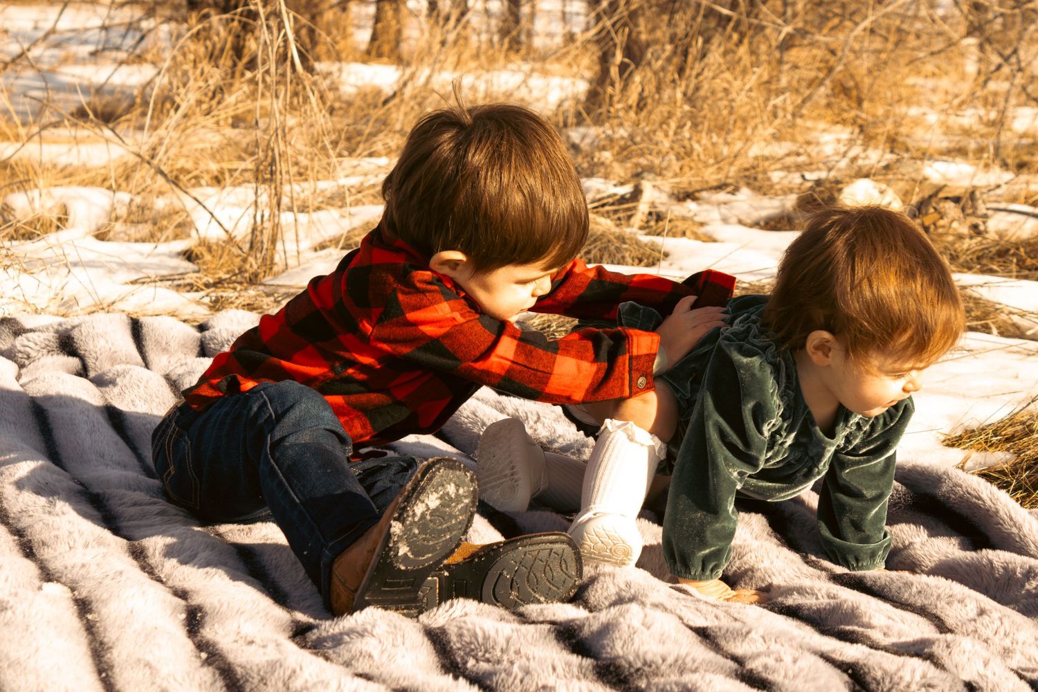 Two children in winter clothing lay on logs outdoors while playing in a sepia-toned vintage photograph.