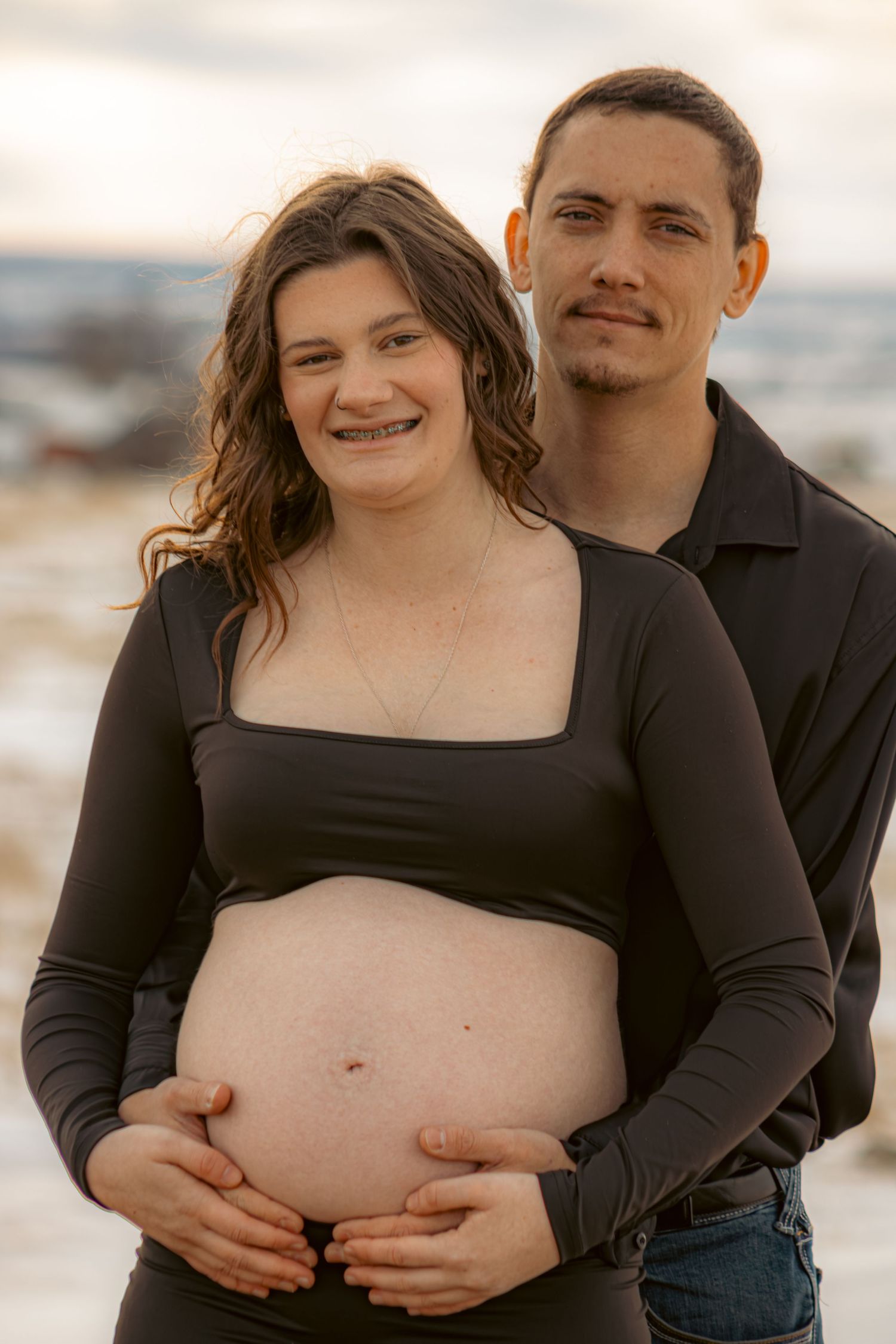 A couple poses together on a beach during a maternity photoshoot at sunset.